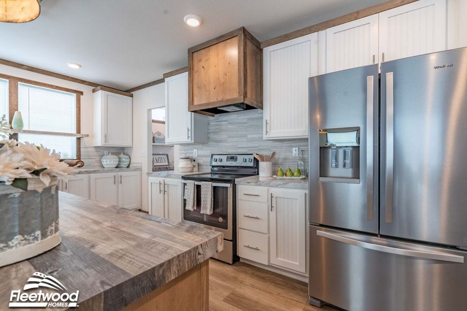 Modern kitchen with stainless steel appliances, including a French door refrigerator and electric range, white cabinetry with wood accents, a rustic wood island, and gray tile backsplash.