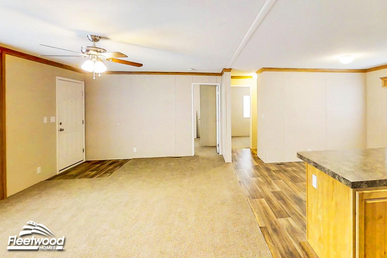 Spacious living room with ceiling fan, carpet, and adjoining wood flooring near kitchen.