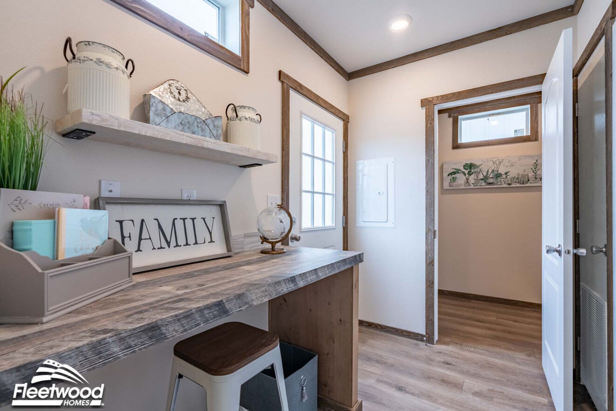 Cozy utility or mudroom area with a rustic wood desk, stool, floating shelf, and farmhouse-style decor, featuring wood trim accents and a door leading outside.