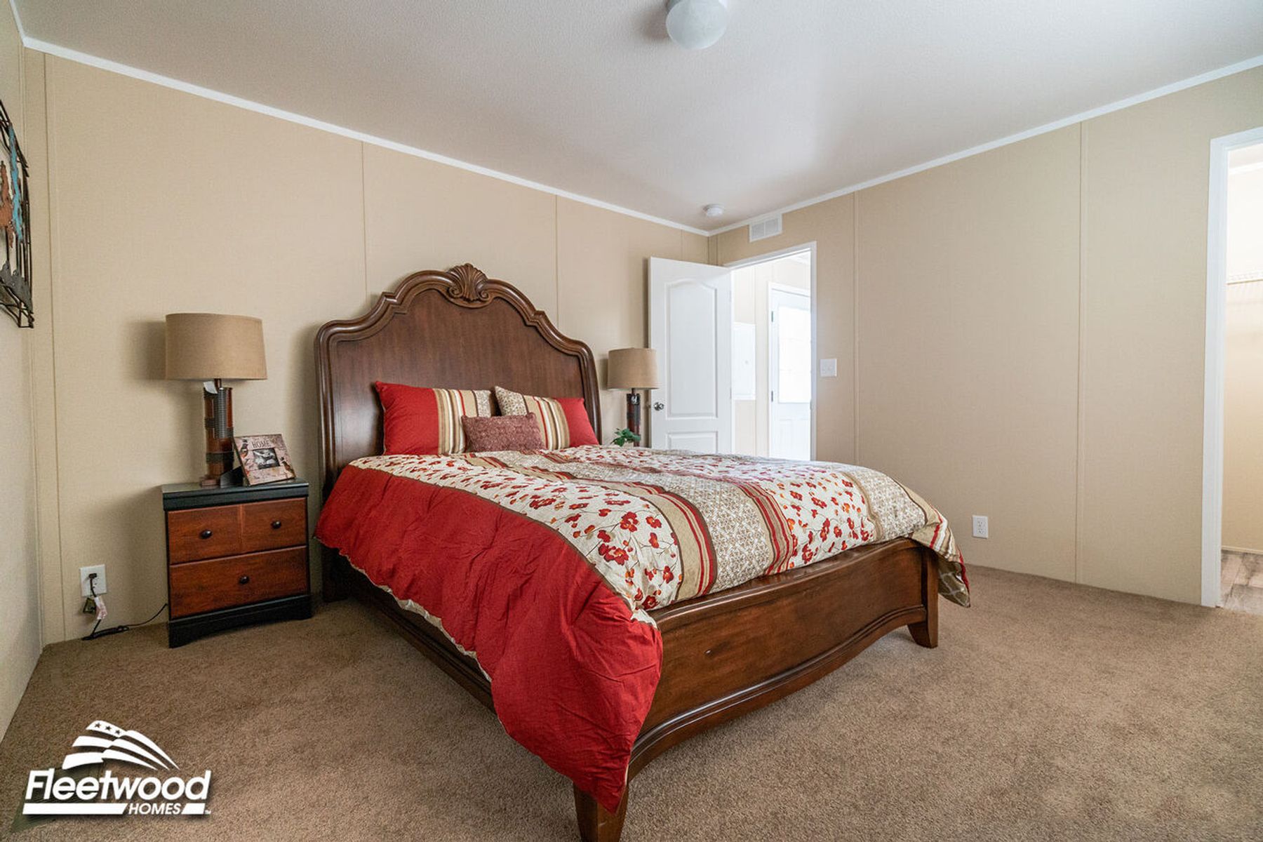 Bedroom with beige walls, carpet flooring, a bed with striped red bedding, and a doorway leading to a bathroom.