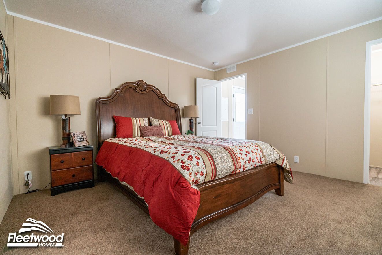 Bedroom with beige walls, carpet flooring, a bed with striped red bedding, and a doorway leading to a bathroom.