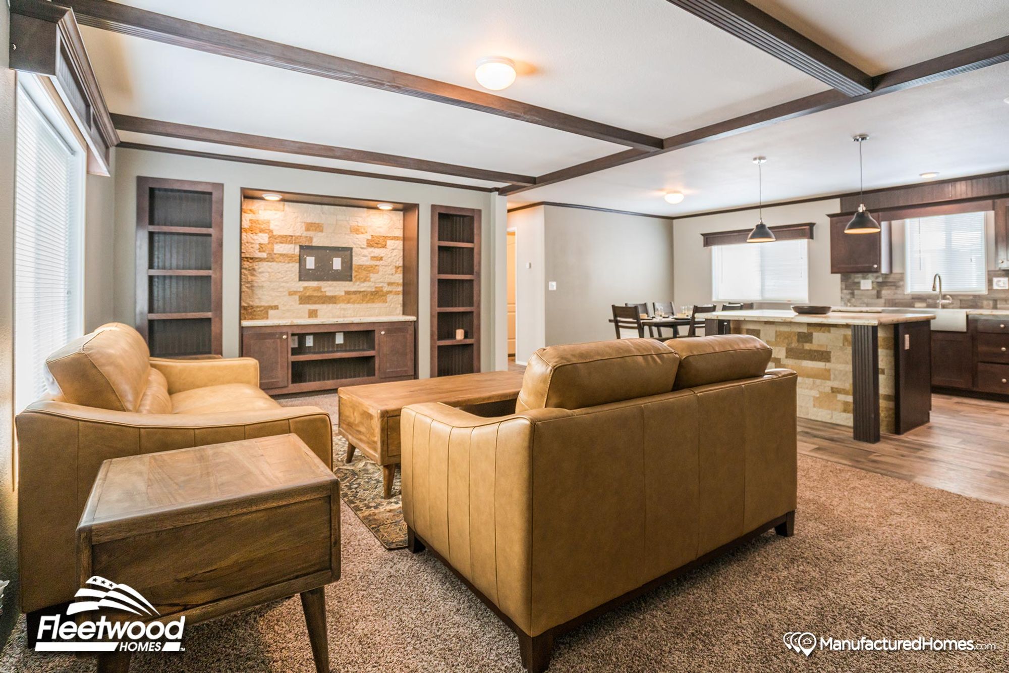 Open-concept living room and kitchen featuring tan leather seating, a built-in entertainment center with stone accent wall, and a modern kitchen island with pendant lighting.