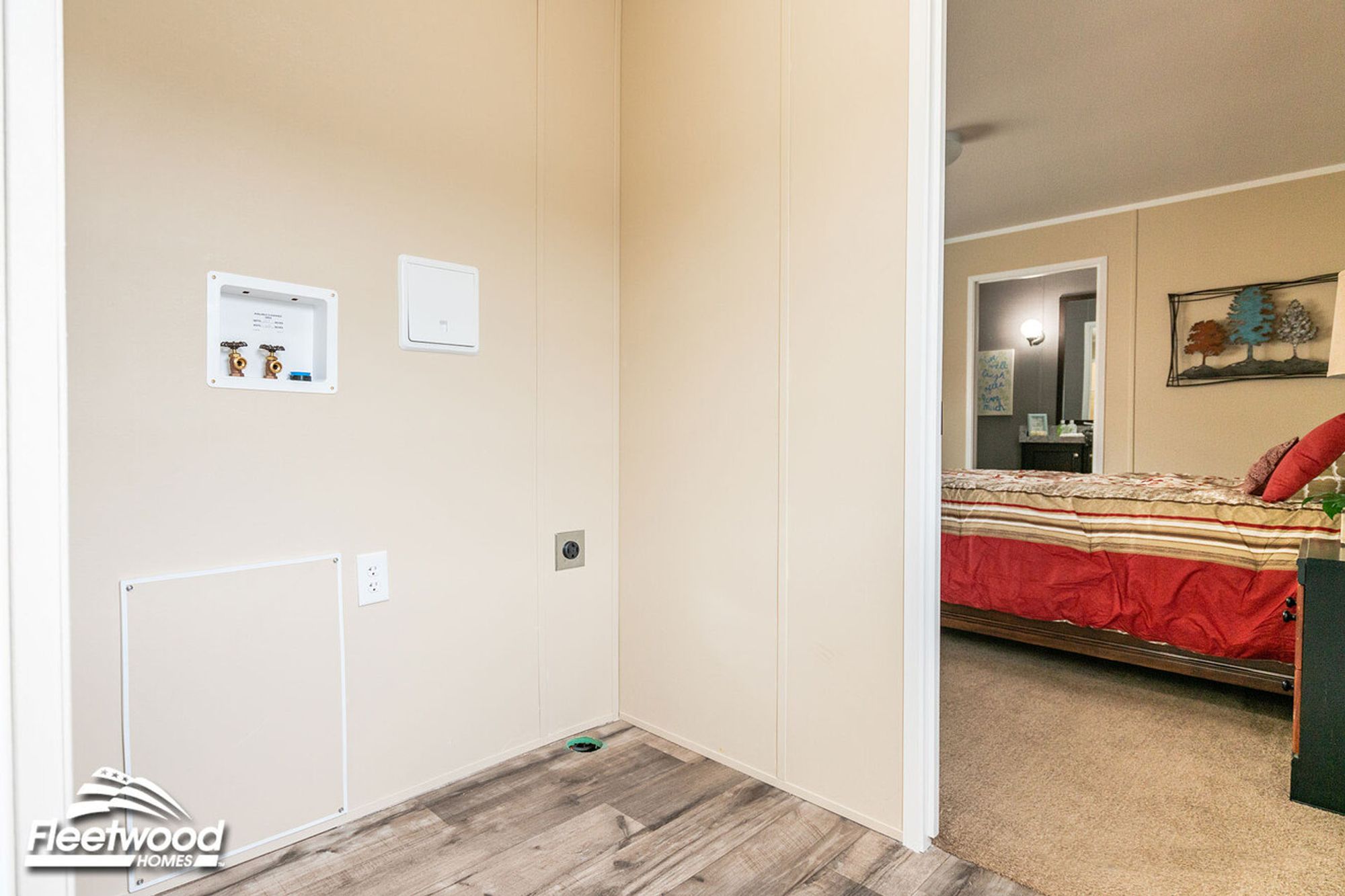 Utility space with washer and dryer hookups, next to a bedroom with a bed and wall art.