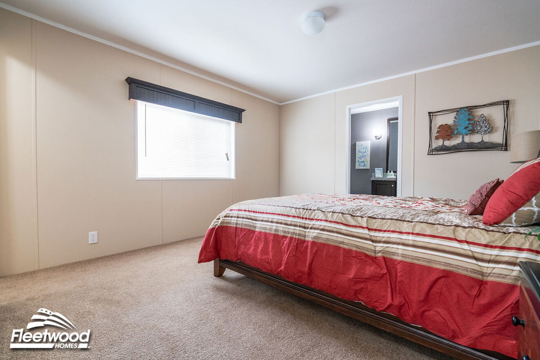 Bedroom with beige walls, carpet flooring, a bed with striped red bedding, and a doorway leading to a bathroom.