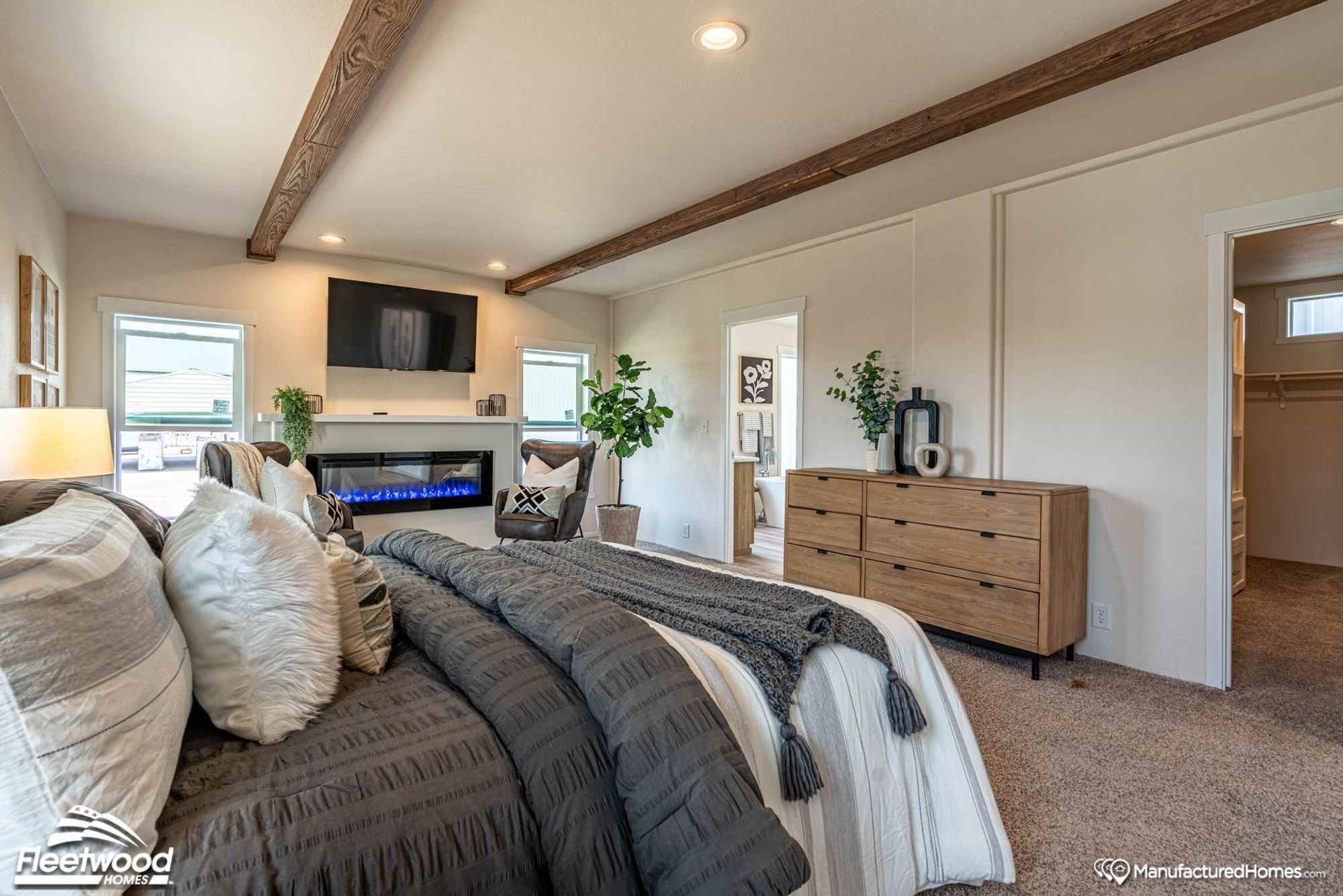 Large bedroom with two chairs, a large bed, and a fire place.