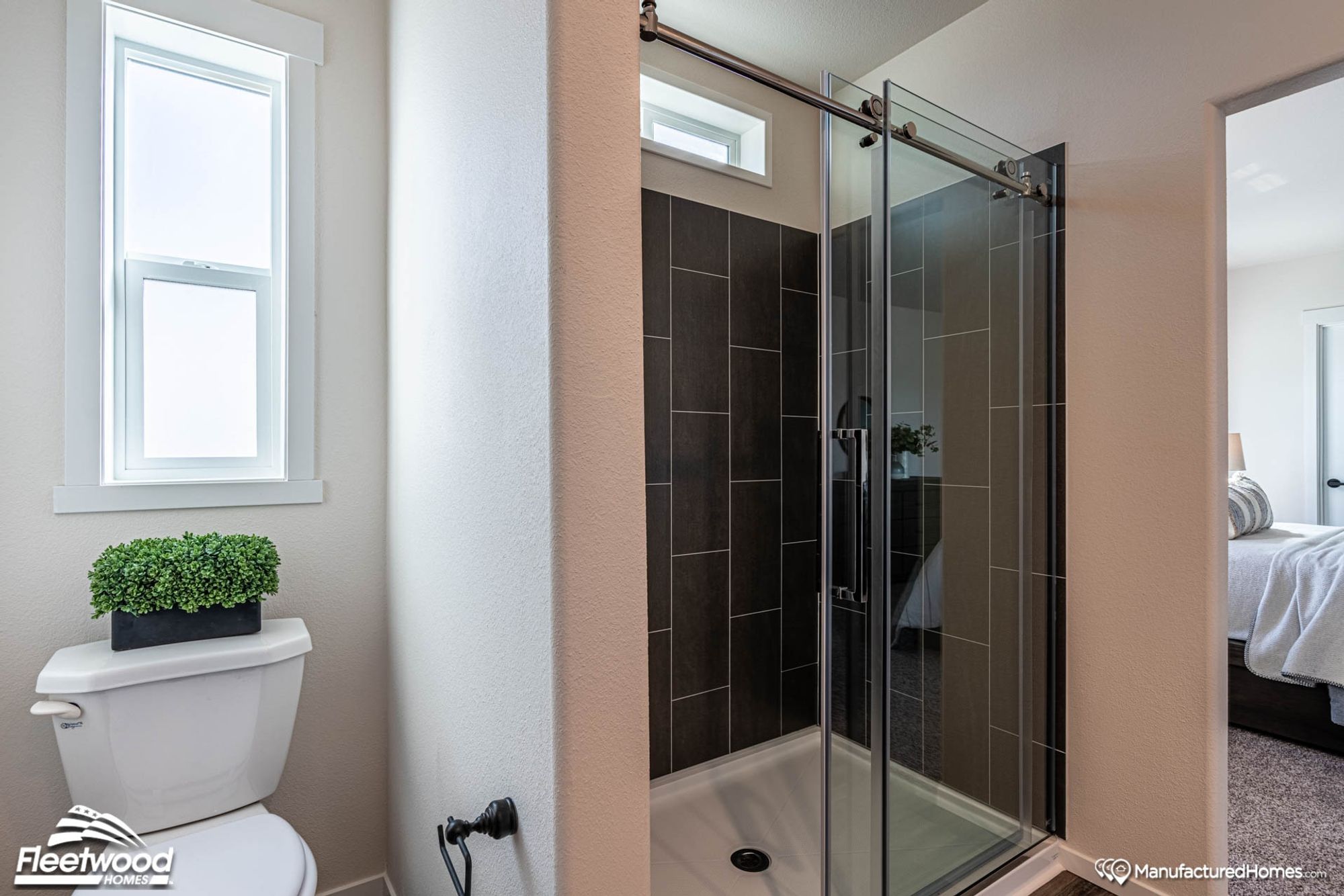 Closer look at a medium-sized standing shower and toilet, with a glimpse into the bedroom.