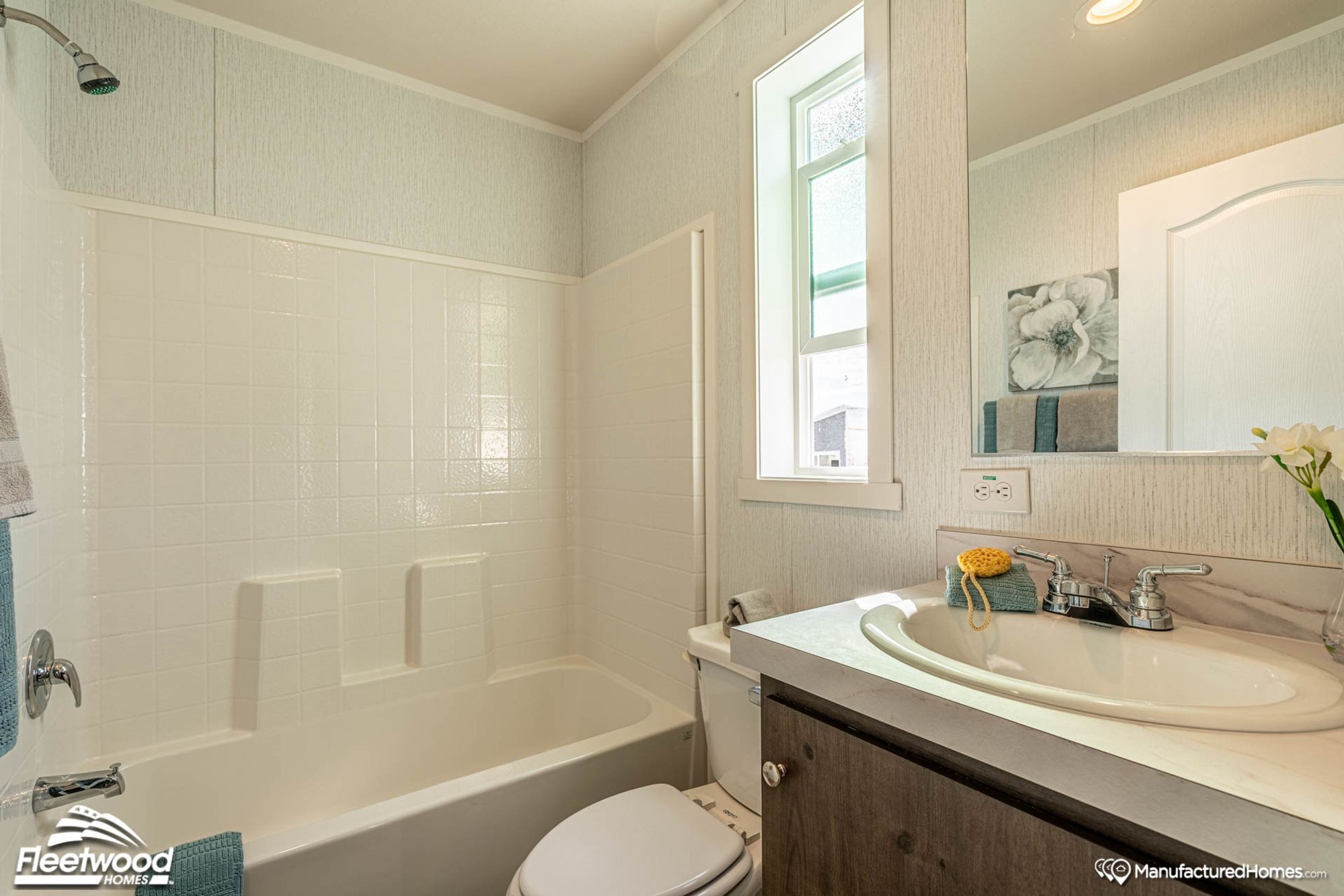 Compact bathroom with a white tile shower-tub combo, single-sink vanity with marble-style countertop, and a tall window providing natural light above the toilet.