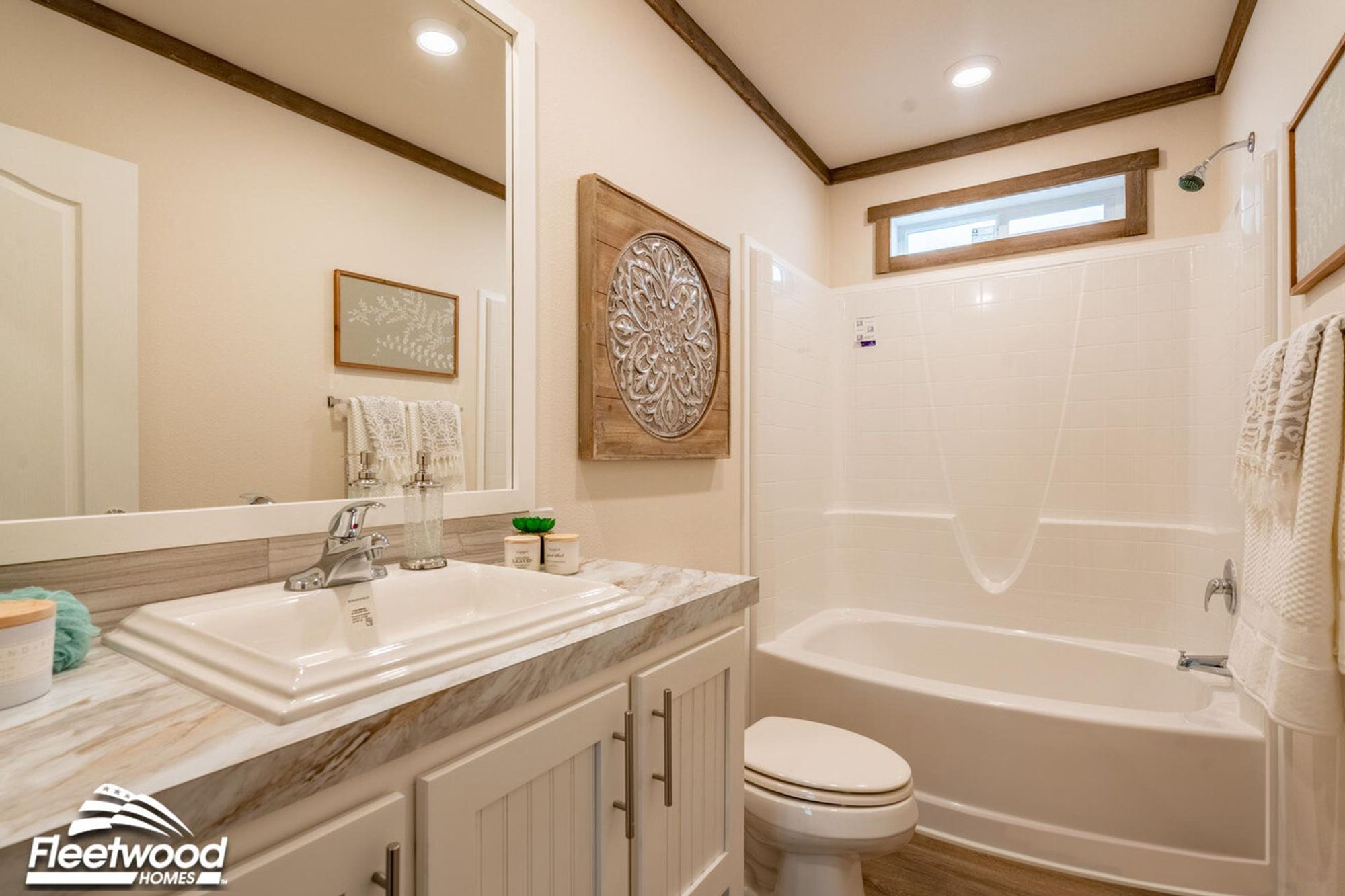 Bright bathroom with a marble-style countertop, rectangular sink, white vanity cabinets, large mirror, and a bathtub-shower combo with white tile surround and decorative wall accents.