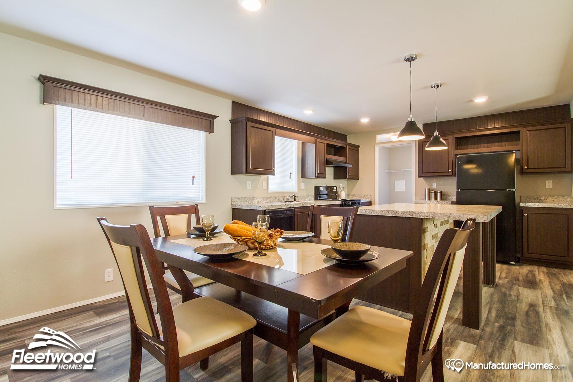 Open kitchen and dining area in a manufactured home, featuring dark wood cabinetry, granite countertops, a set dining table, and pendant lighting over the island.