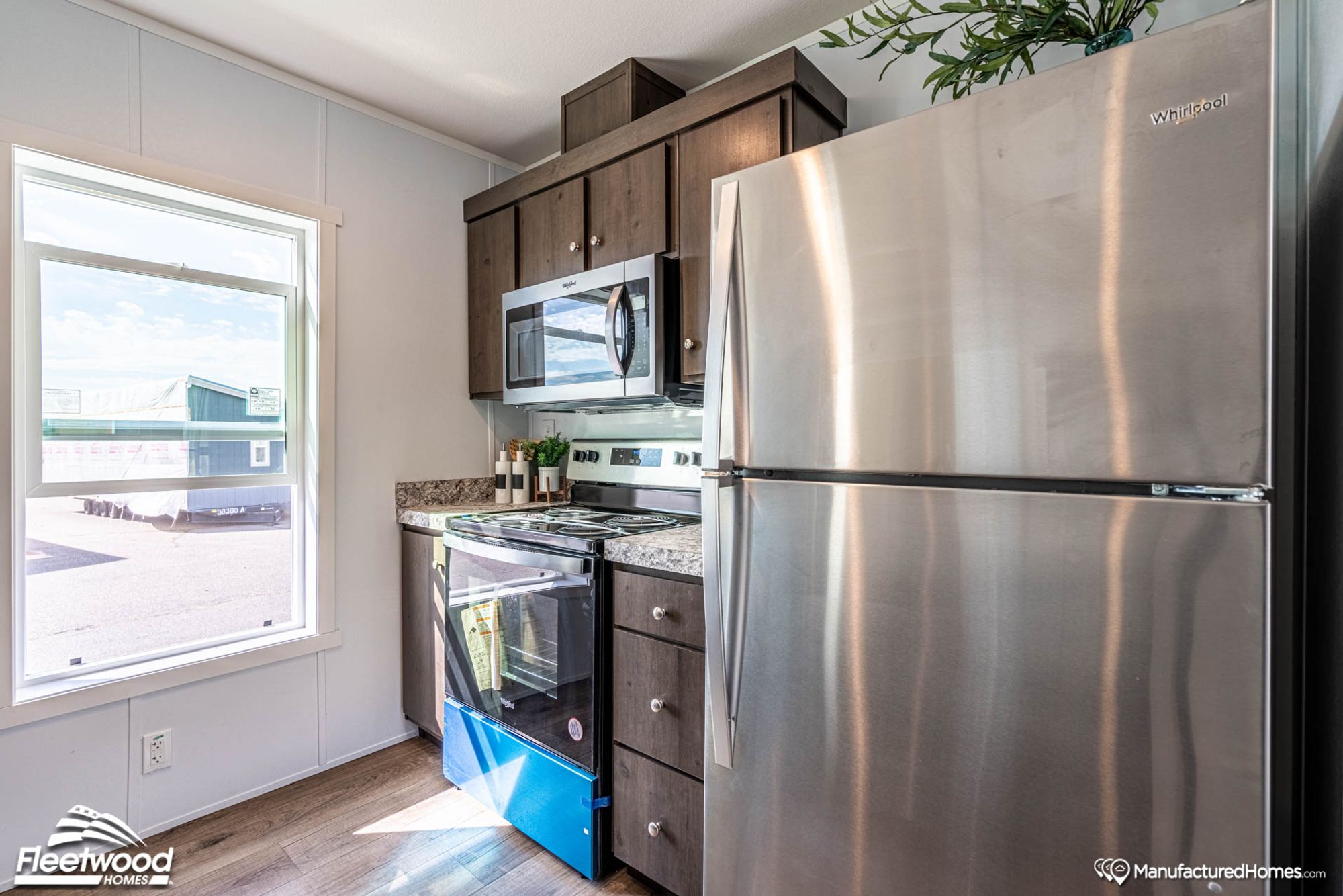 Compact kitchen with stainless steel Whirlpool appliances, including a microwave, electric stove, and refrigerator, set against dark wood cabinetry and marbled countertops.