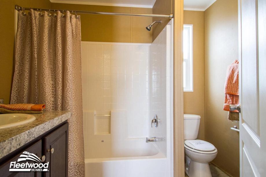 Bathroom with shower-tub combo, patterned curtain, toilet, and vanity with granite-style countertop.