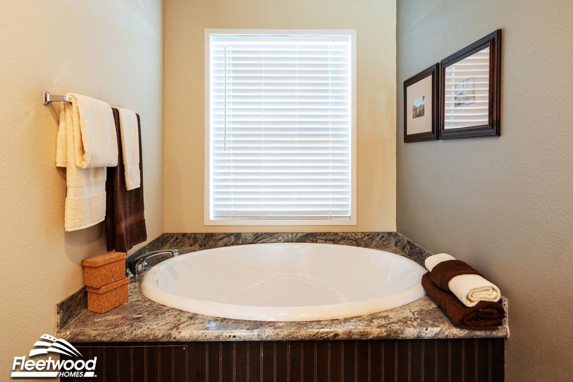 Bathroom with a large corner soaking tub set in a granite surround, accented by wall art and neatly folded towels.