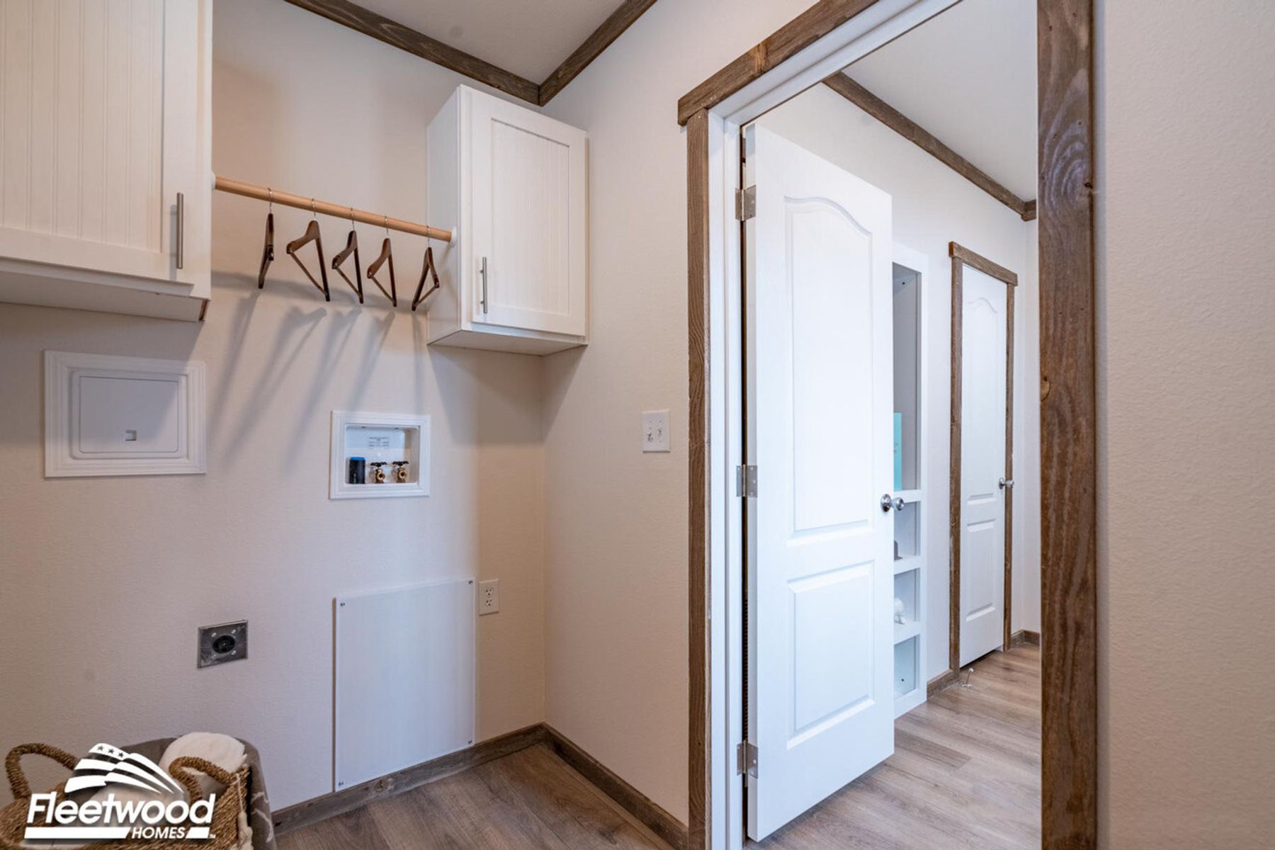 Laundry room with wood-look flooring, white cabinets, a hanging rod with wooden hangers, utility hookups, and a basket of towels.