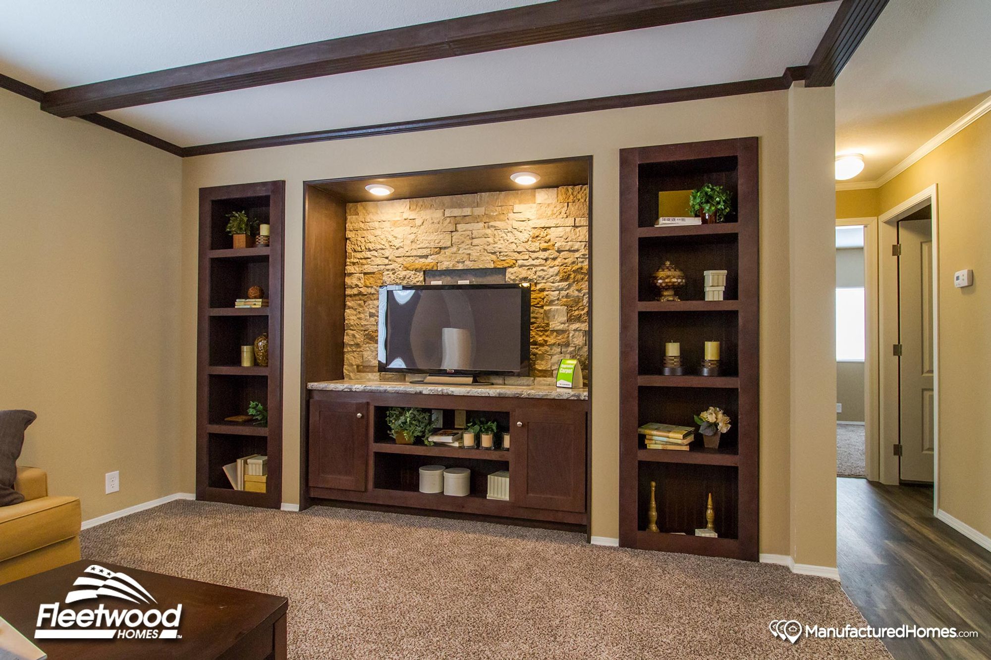 Living room entertainment center with built-in dark wood shelving, a mounted TV, stone accent wall with recessed lighting, and decorative items arranged throughout.