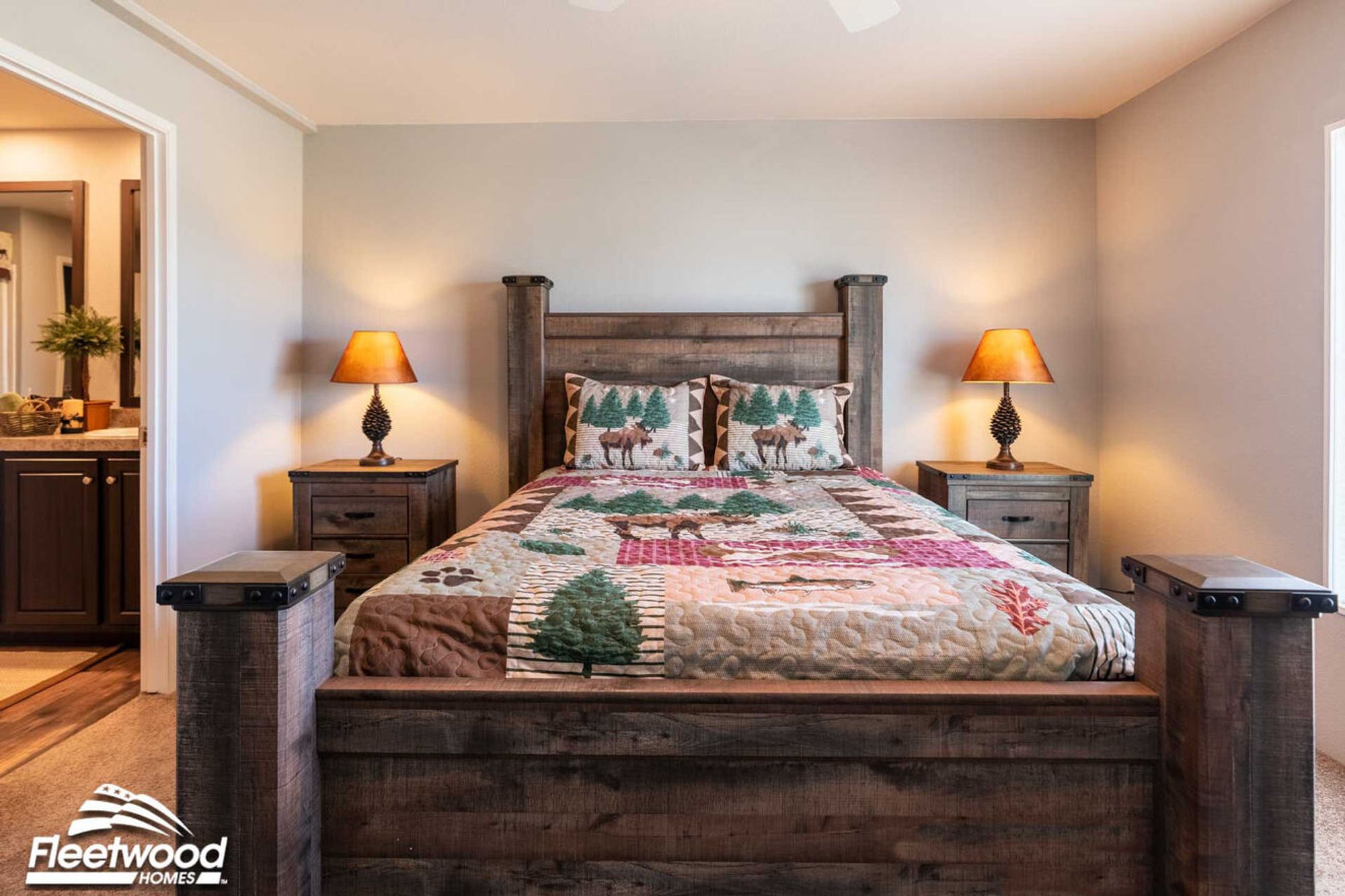 Rustic-style bedroom with a wooden bed frame, forest-themed quilt and pillows featuring moose and trees, flanked by two matching nightstands with pinecone-shaped lamps.