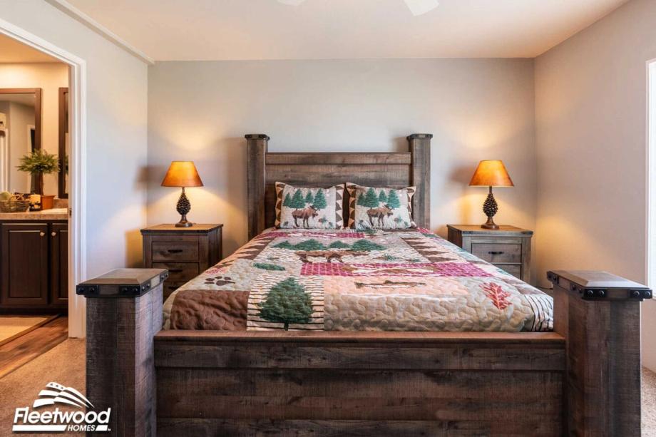 Rustic-style bedroom with a wooden bed frame, forest-themed quilt and pillows featuring moose and trees, flanked by two matching nightstands with pinecone-shaped lamps.