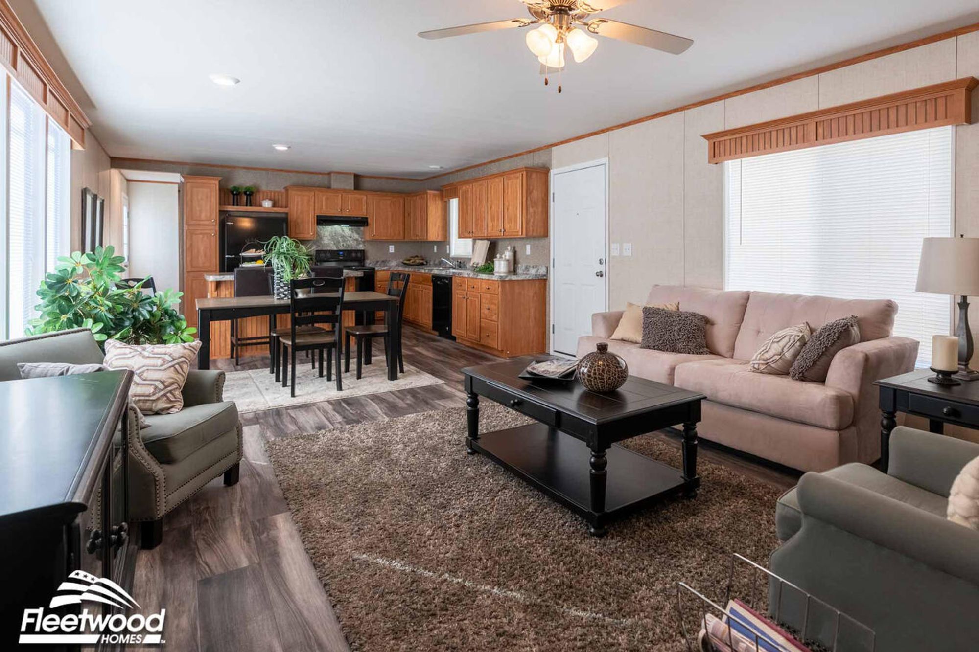 Cozy living room with a beige sofa, two gray armchairs, a dark wood coffee table, and wall art accents under a ceiling fan.
