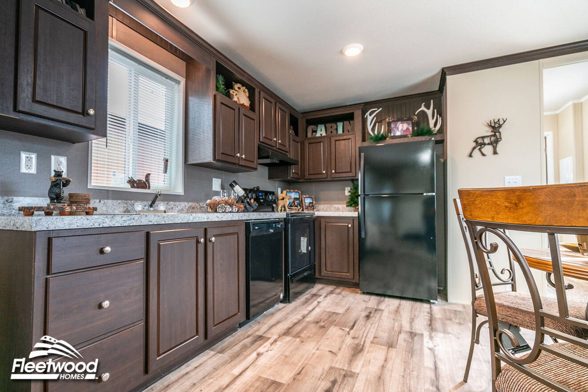Dining area with a round table and chairs next to a kitchen featuring dark wood cabinets, granite-style countertops, and black appliances.
