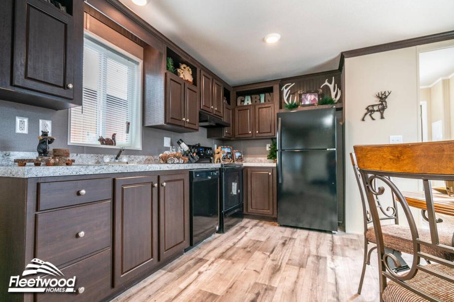 Dining area with a round table and chairs next to a kitchen featuring dark wood cabinets, granite-style countertops, and black appliances.