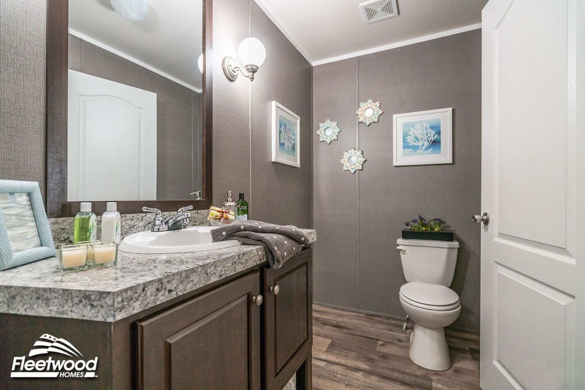 Bathroom with gray walls, a granite-style vanity, dark wood cabinets, a toilet, and coastal-themed wall art.