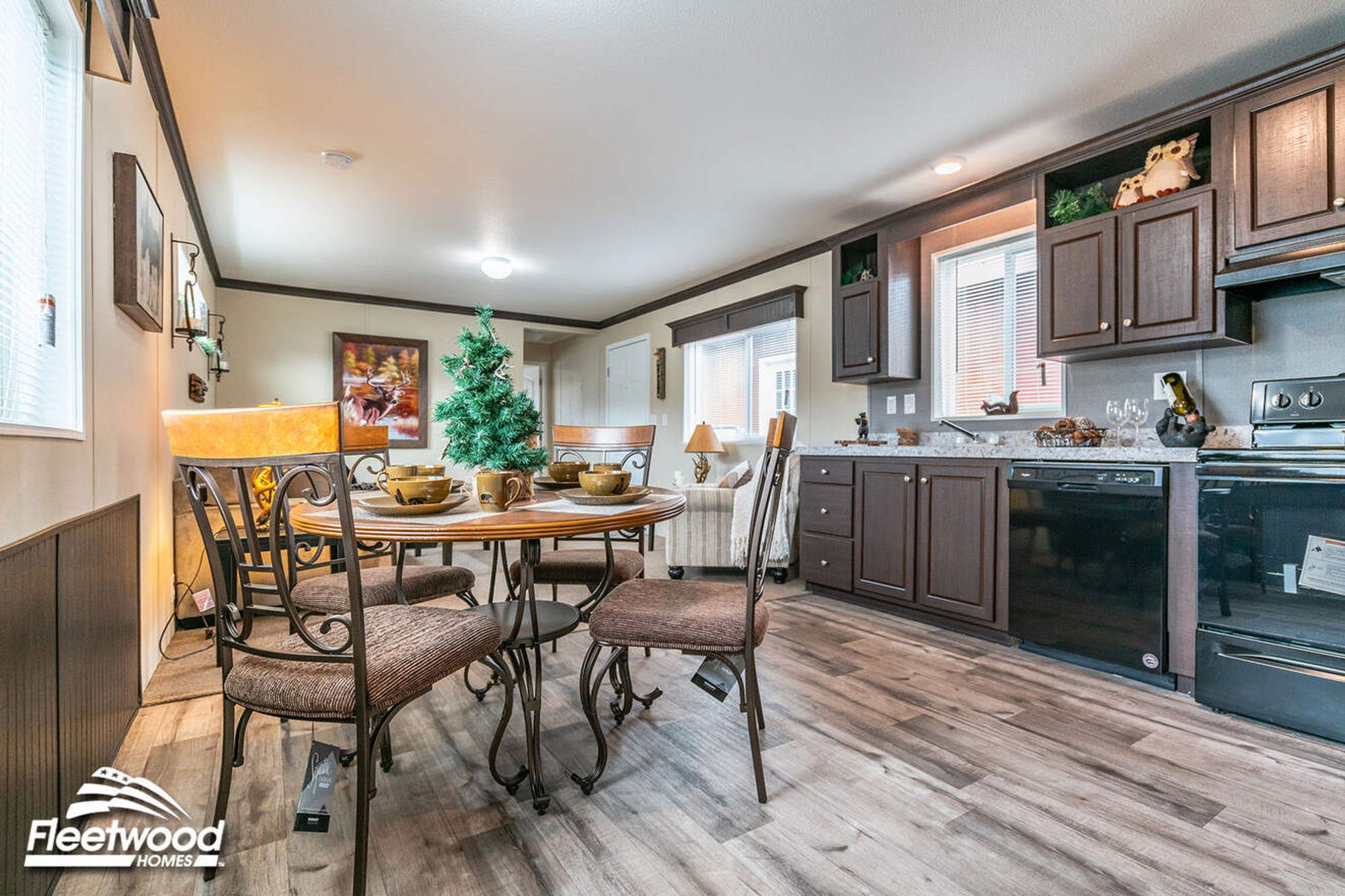 Dining area with a round table and chairs next to a kitchen featuring dark wood cabinets, granite-style countertops, and black appliances.