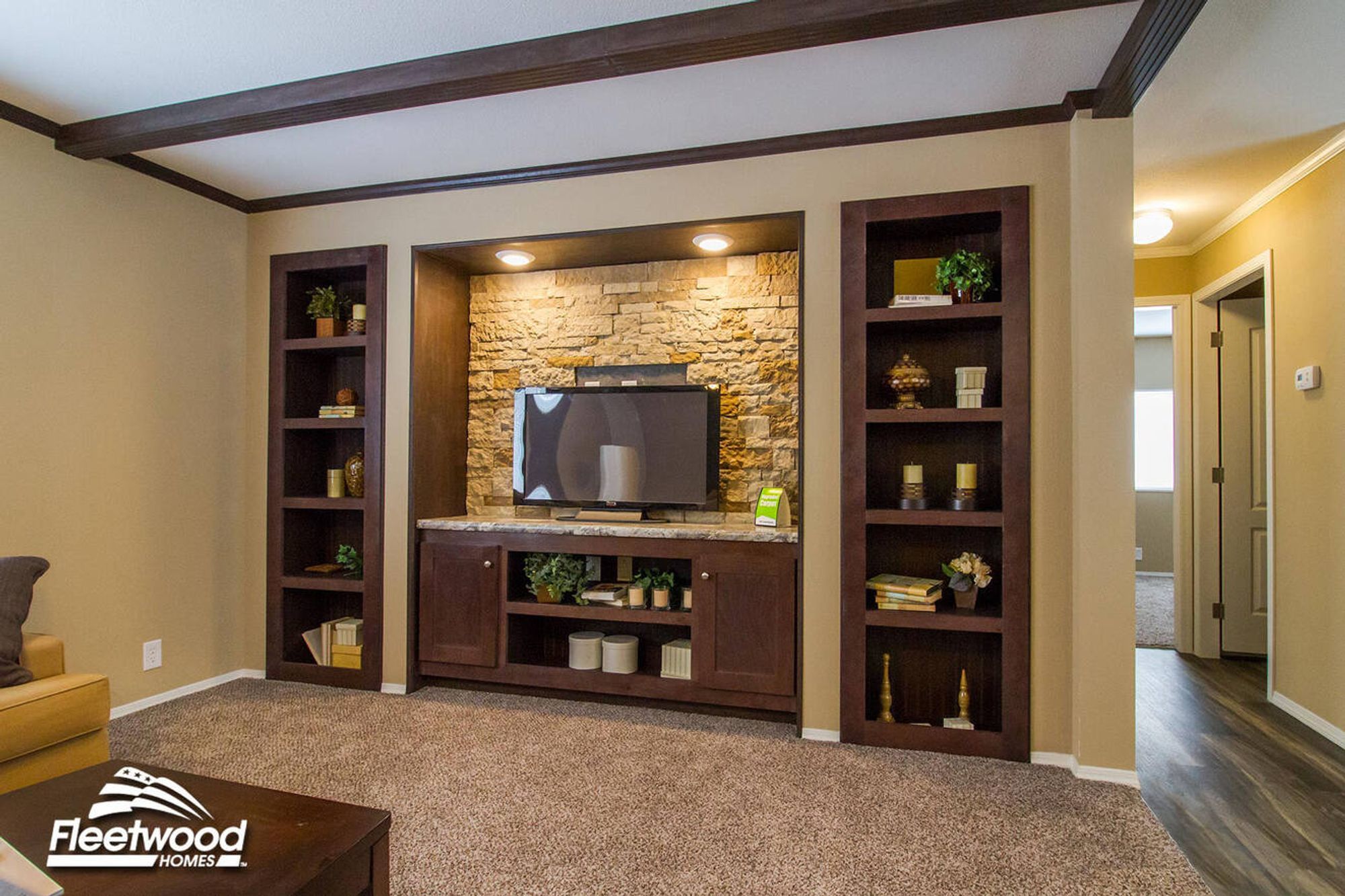 Living room entertainment center with a stone accent wall, built-in shelving, and a flat-screen TV framed by dark wood cabinetry and decor.