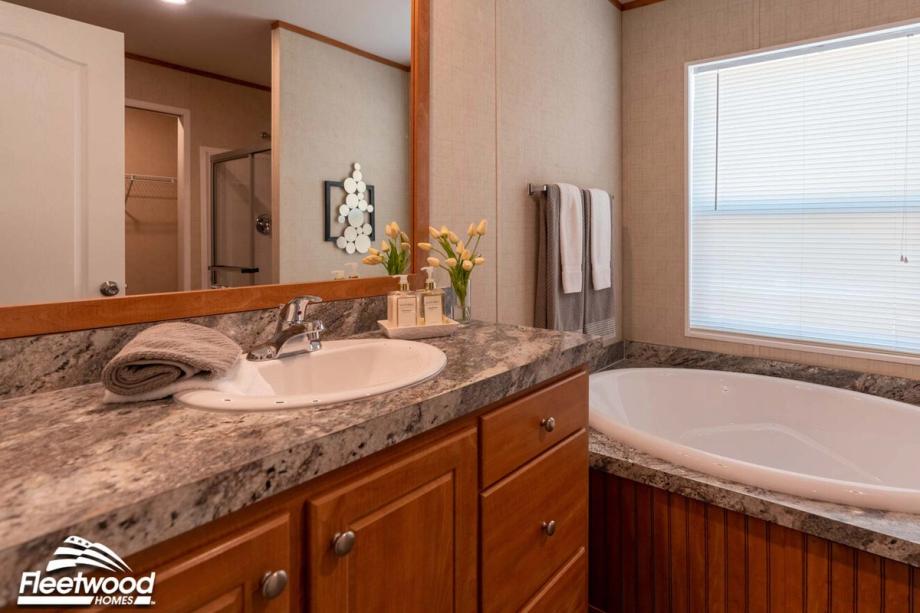 Bathroom with granite-style vanity, built-in sink, soaking tub under a window, and a mirror reflecting the shower and closet.