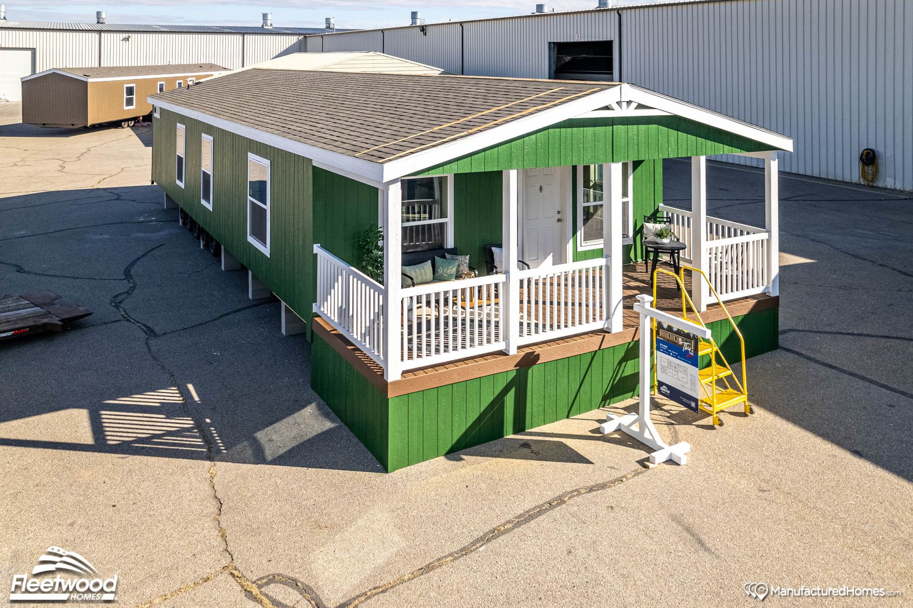 Covered front porch with green siding, outdoor seating, a small table, rug, and potted plant. White front door and railing, with neighboring homes visible in the background.