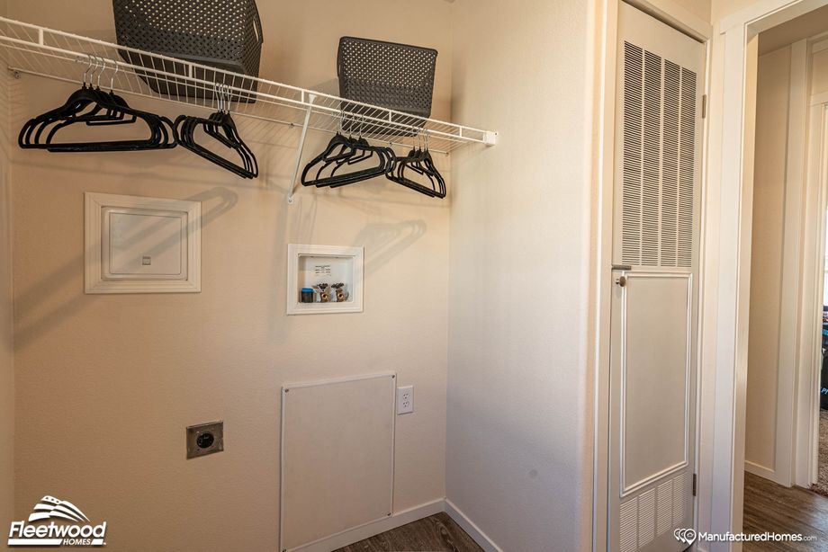 Utility or laundry room with hookups for a washer and dryer, wire shelving above with black clothes hangers and storage bins, and a vented door likely concealing a water heater or HVAC unit.