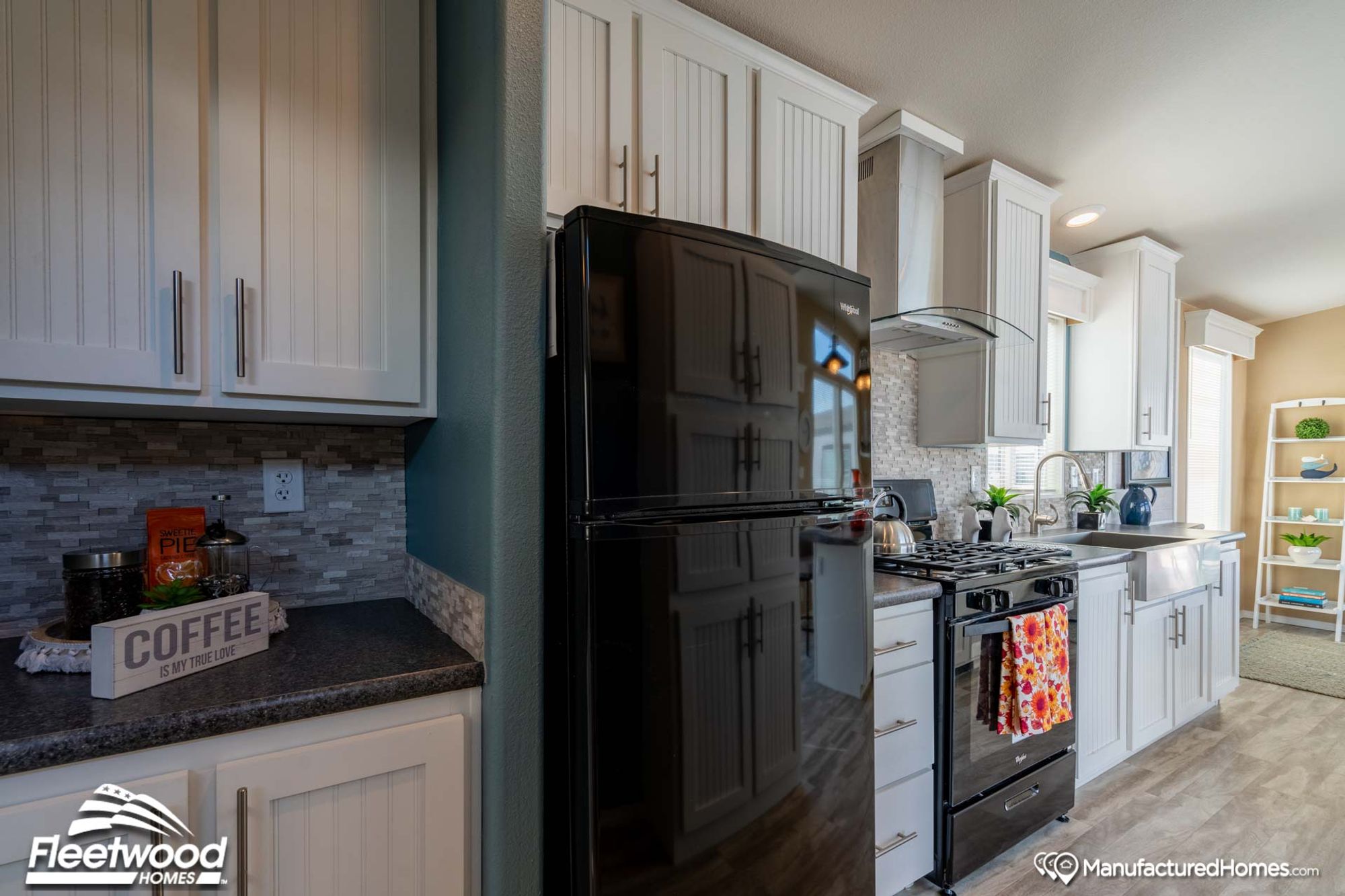 Modern kitchen with white shaker cabinets, gray tile backsplash, black Whirlpool refrigerator, matching gas stove, and farmhouse sink with chrome faucet.