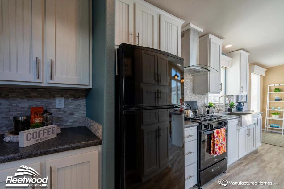 Modern kitchen with white shaker cabinets, gray tile backsplash, black Whirlpool refrigerator, matching gas stove, and farmhouse sink with chrome faucet.