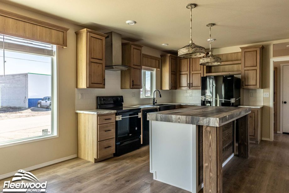 Kitchen with natural wood cabinetry, black appliances, farmhouse sink, and a rustic wood island with pendant lighting.