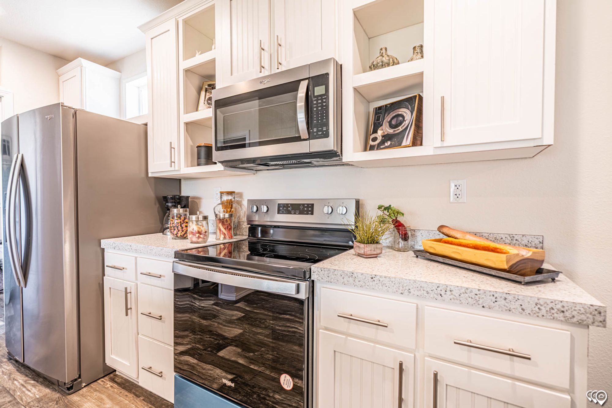 Close-up view of a kitchen with white cabinets, a refrigerator, overhead microwave, and oven.