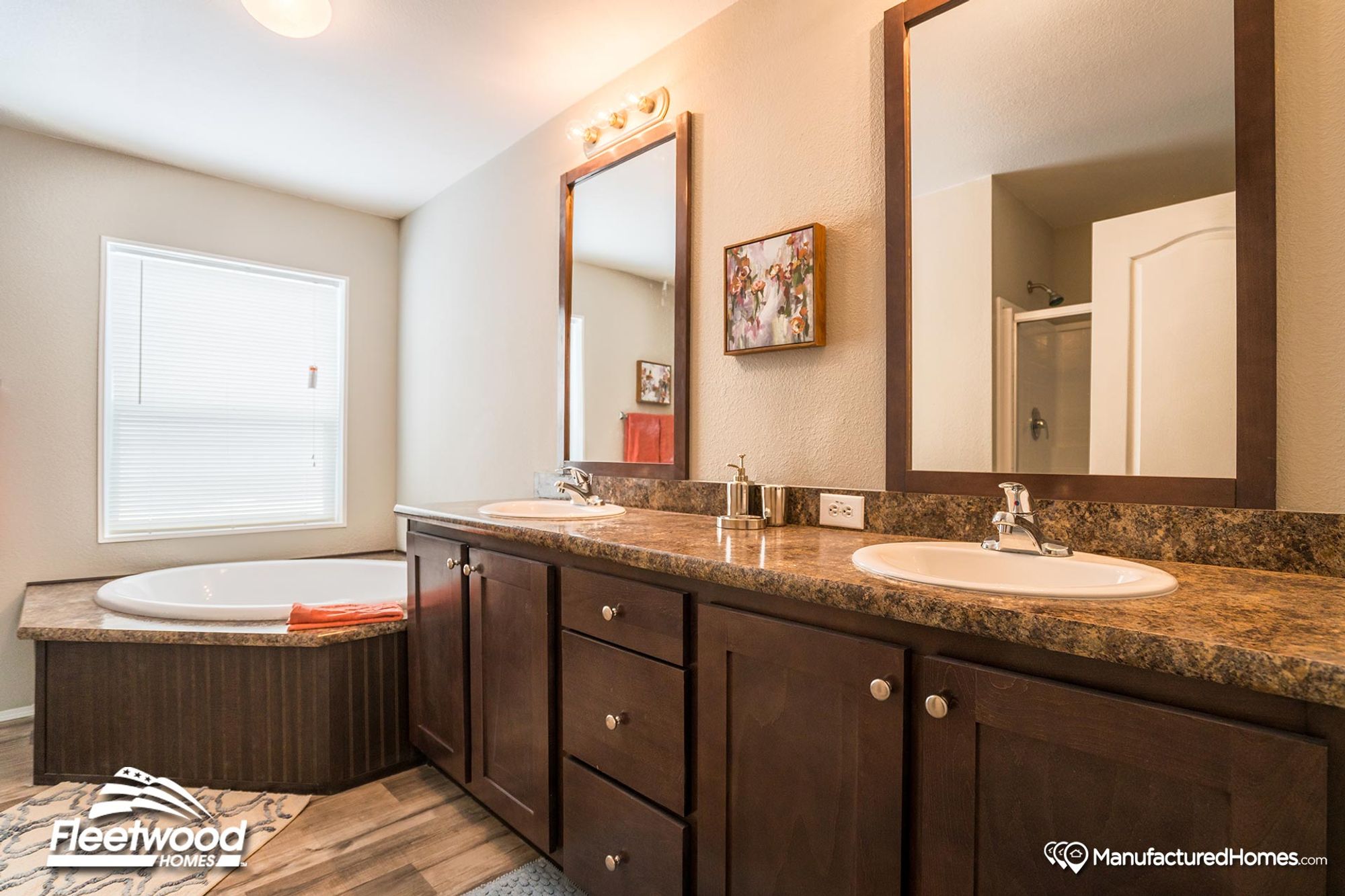 Elegant bathroom featuring a dual-sink vanity with dark wood cabinets, granite countertops, a large soaking tub by the window, and two framed mirrors above the sinks.