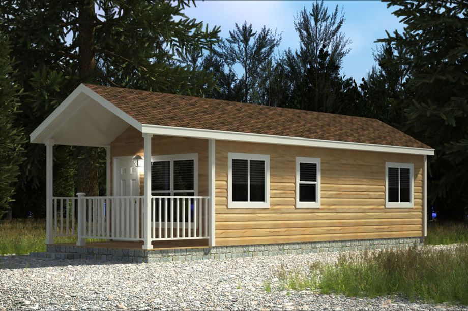 Exterior view of a small manufactured home with wood-look siding, a gable roof, white trim, and a covered front porch with railing. Surrounded by trees and gravel landscaping.