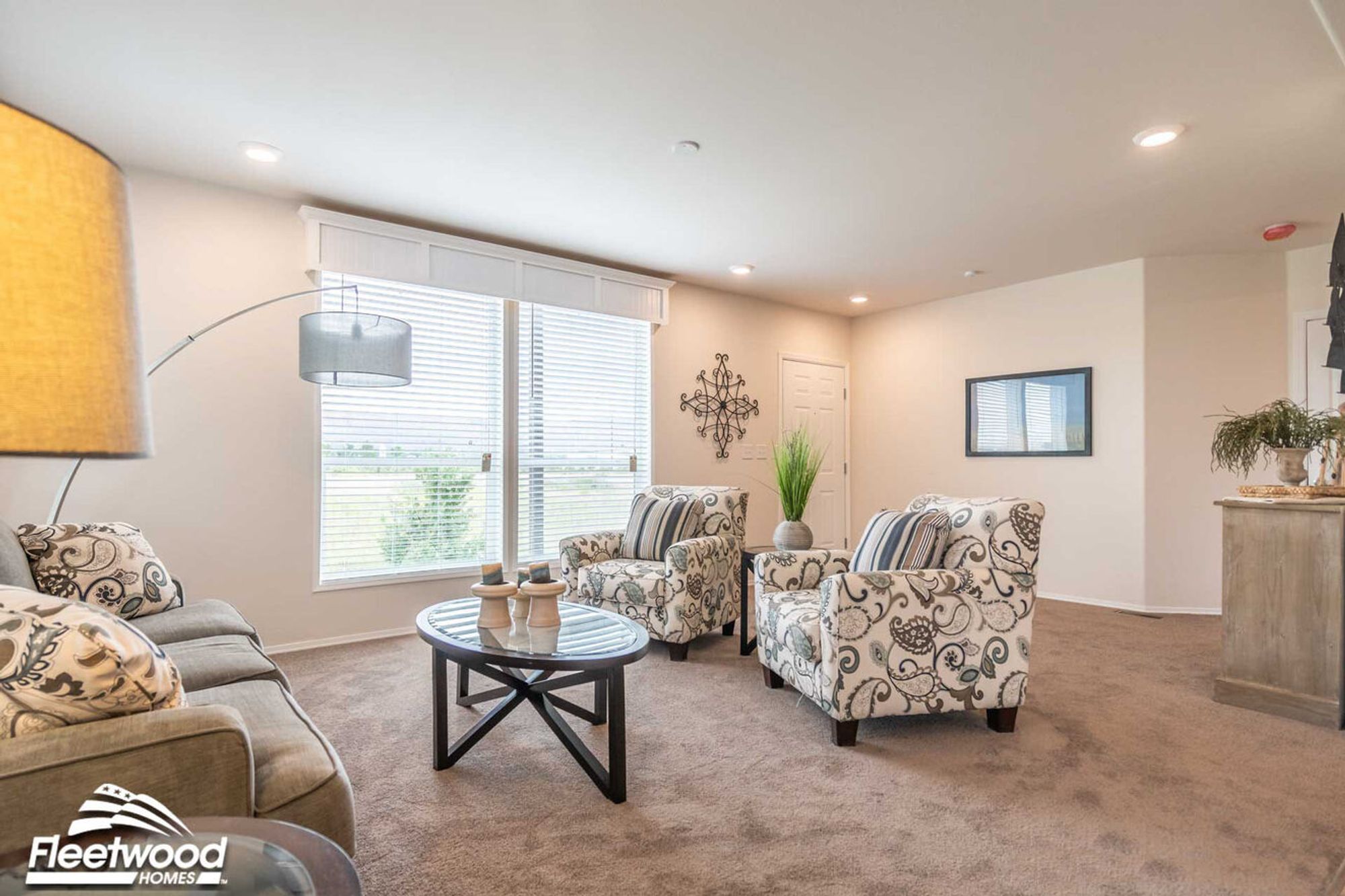 Open living space with patterned armchairs, glass coffee table, and view into a modern kitchen with bar seating and dining area.