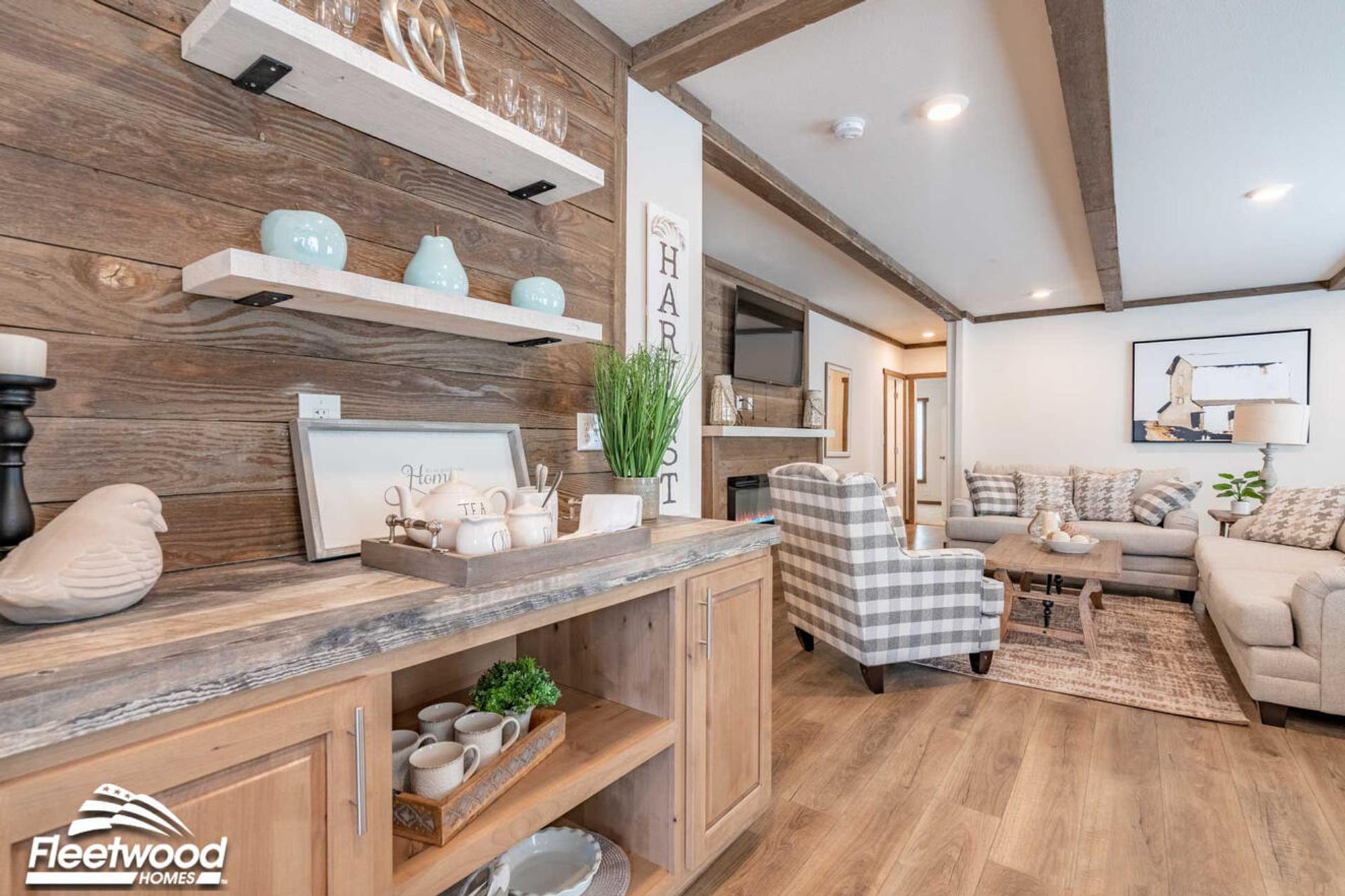 Rustic living area with wood-paneled accent wall, floating shelves, and a built-in cabinet for storage, opening into a cozy seating area with plaid and neutral-toned furniture.
