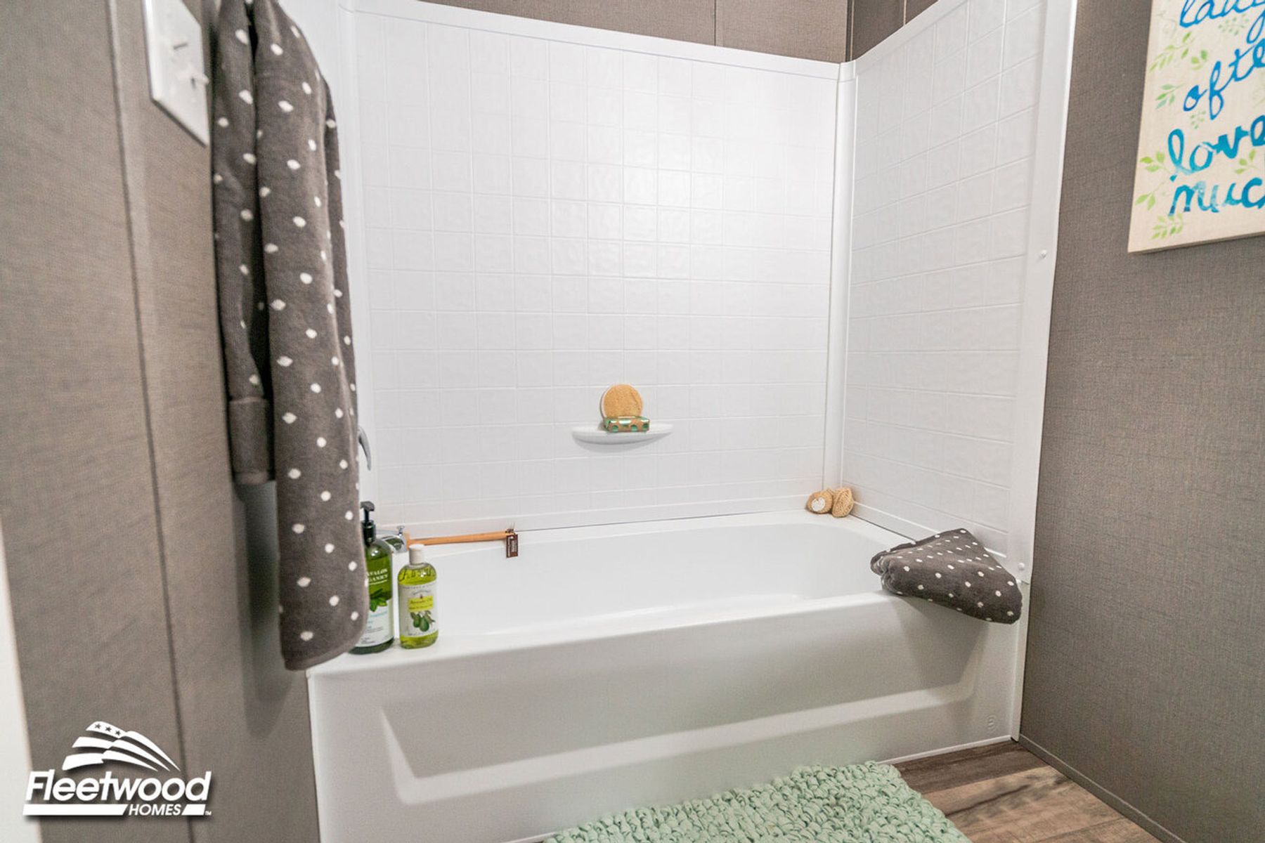 Bathroom with a white bathtub and shower combo, gray walls, and a green rug on the wood-style floor.
