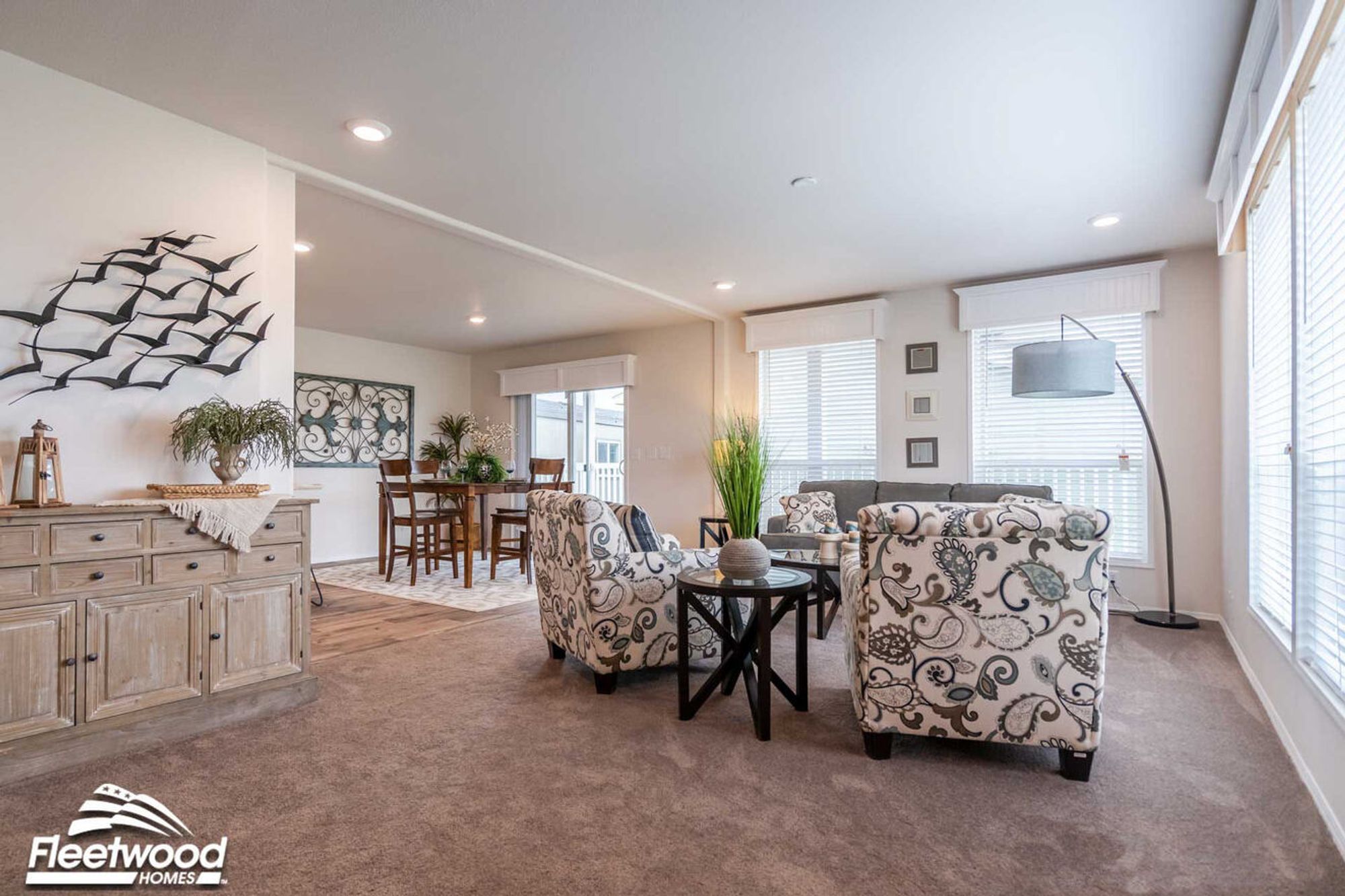 Open living space with patterned armchairs, glass coffee table, and view into a modern kitchen with bar seating and dining area.