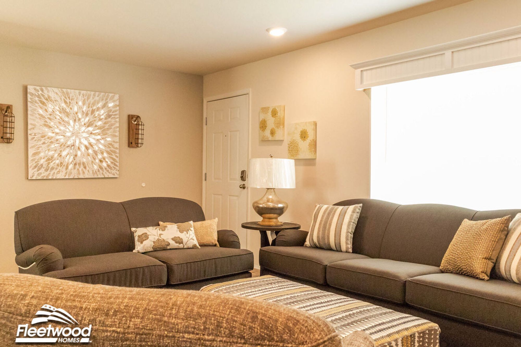 Warm-toned living room with brown sofas, striped throw pillows, a round side table with a glass lamp, and soft ambient wall art and lighting.