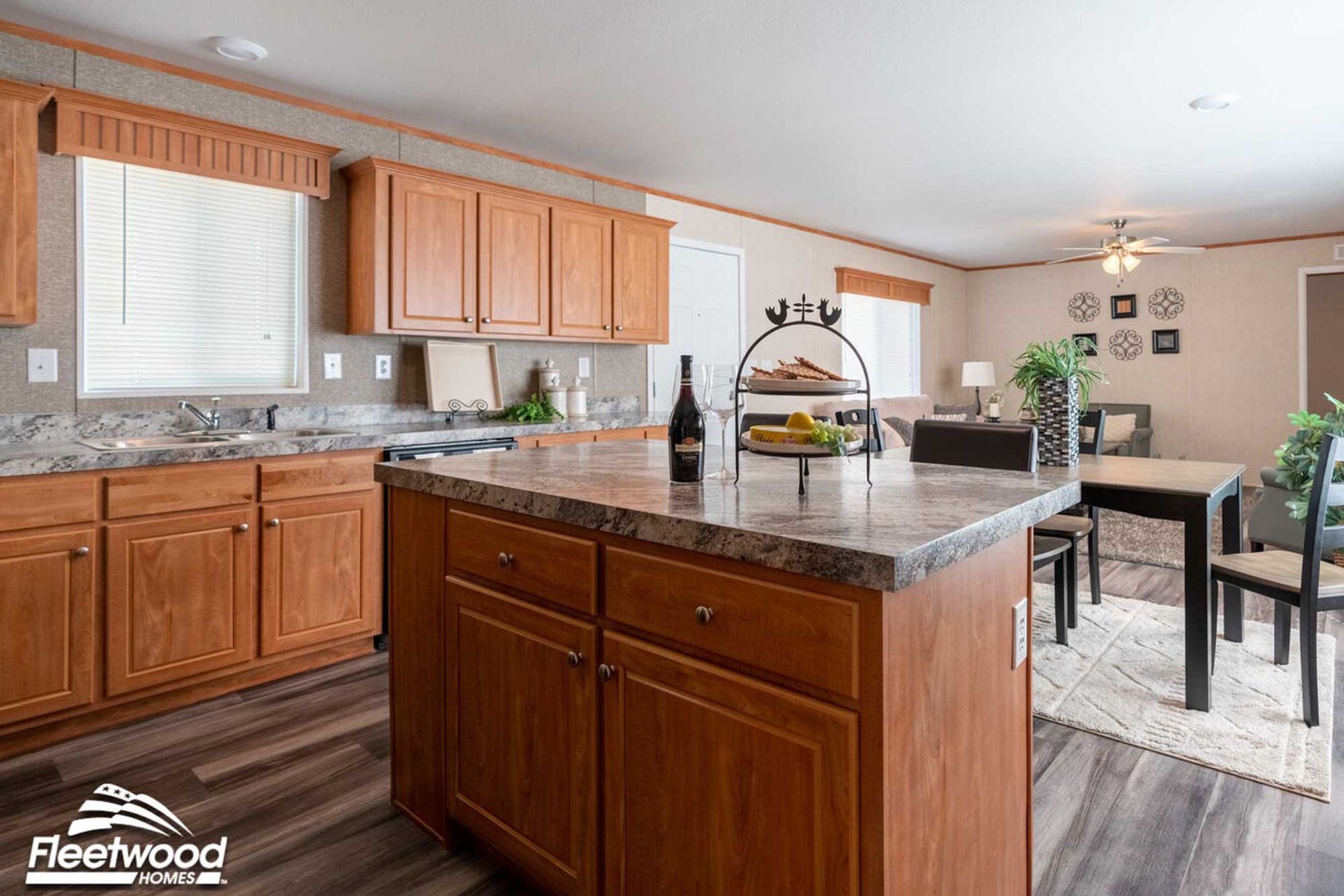 Kitchen with wood cabinets, marble-style countertops, and a central island overlooking the dining and living area.