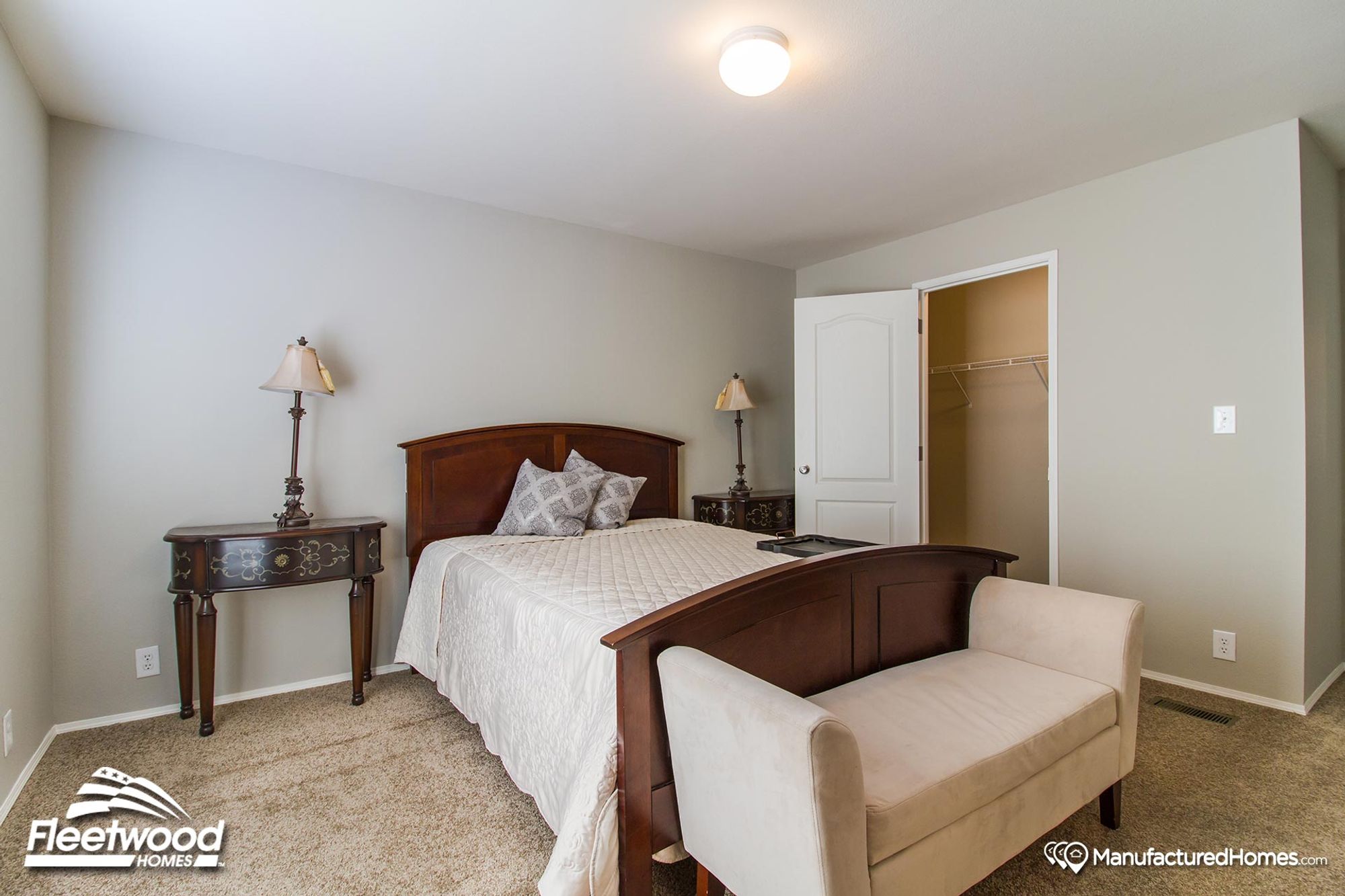 Bright bedroom with neutral tones, featuring a dark wood bed frame, cream quilted bedding, an upholstered bench at the foot of the bed, and vintage-style nightstands.