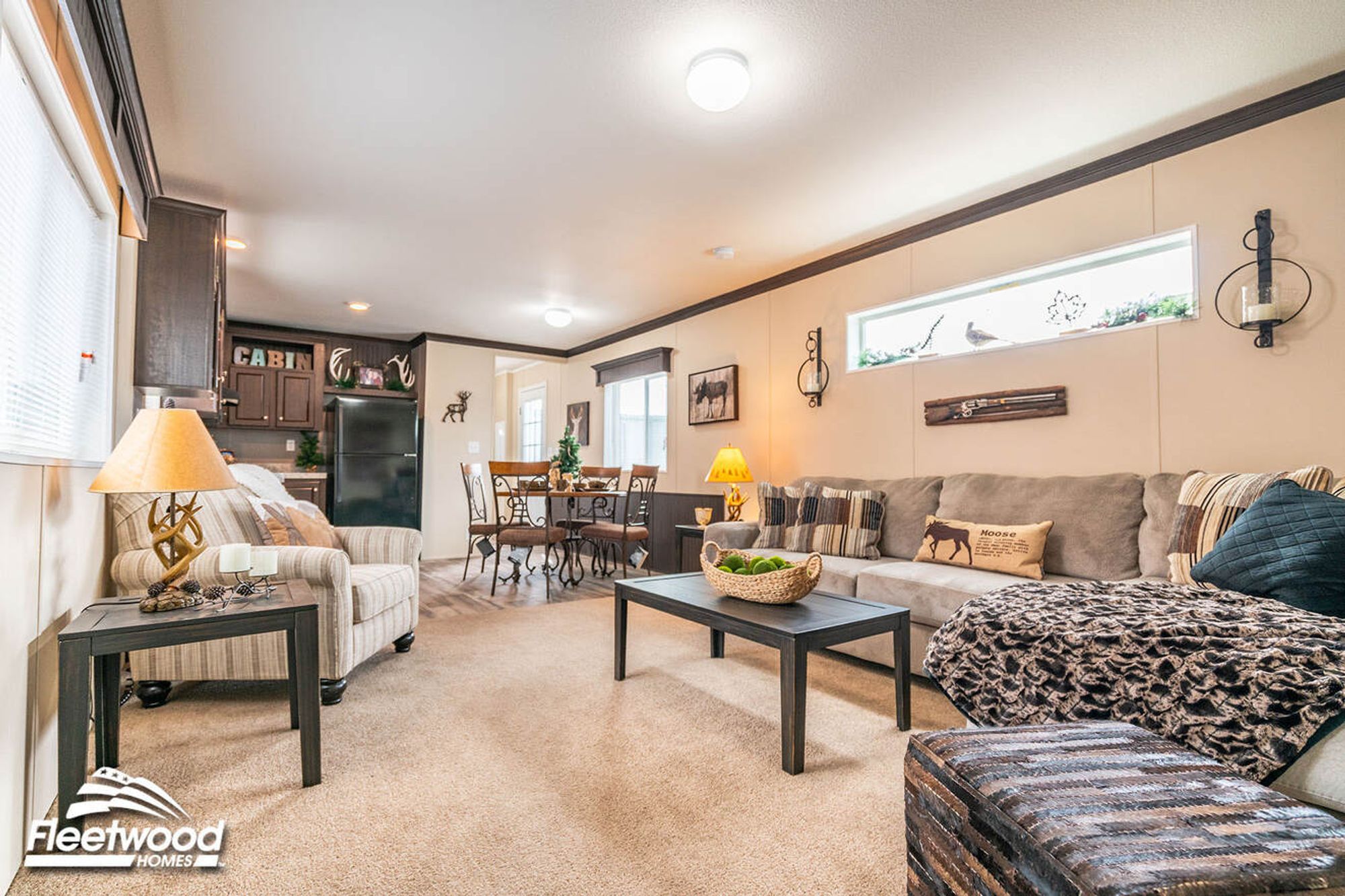 Open living and dining area with a sectional sofa, rustic decor, dark wood coffee table, and a round dining set near the kitchen.