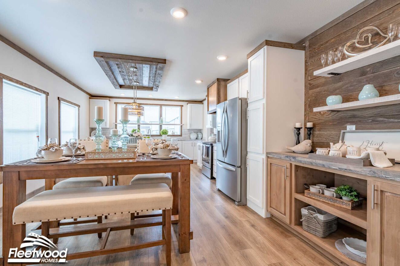 Open-concept kitchen and dining area with a rustic wood island, pendant lighting, wood-look flooring, and large windows, flowing into a living room with a sectional sofa.