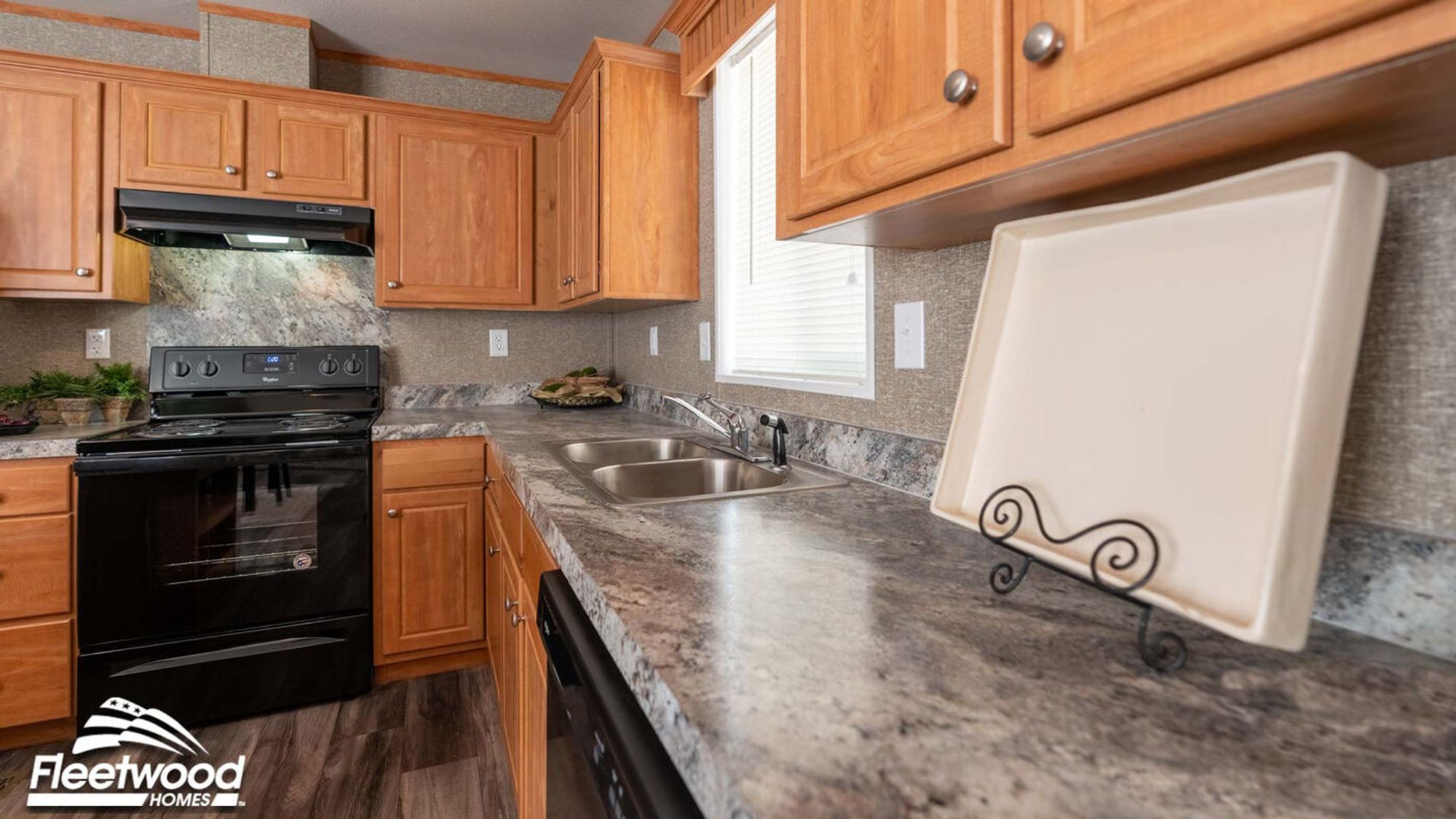 Kitchen with wood cabinets, marble-look countertops, a black stove with matching range hood, and a double sink beneath a window.