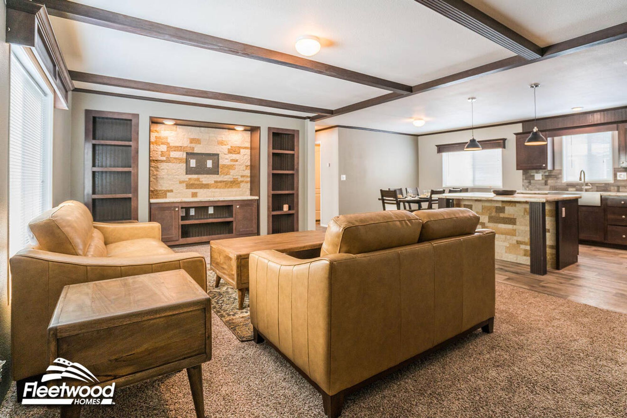 Open-concept living space with tan leather sofas, built-in entertainment center with stone accent wall, and a view of the adjacent kitchen and dining area.