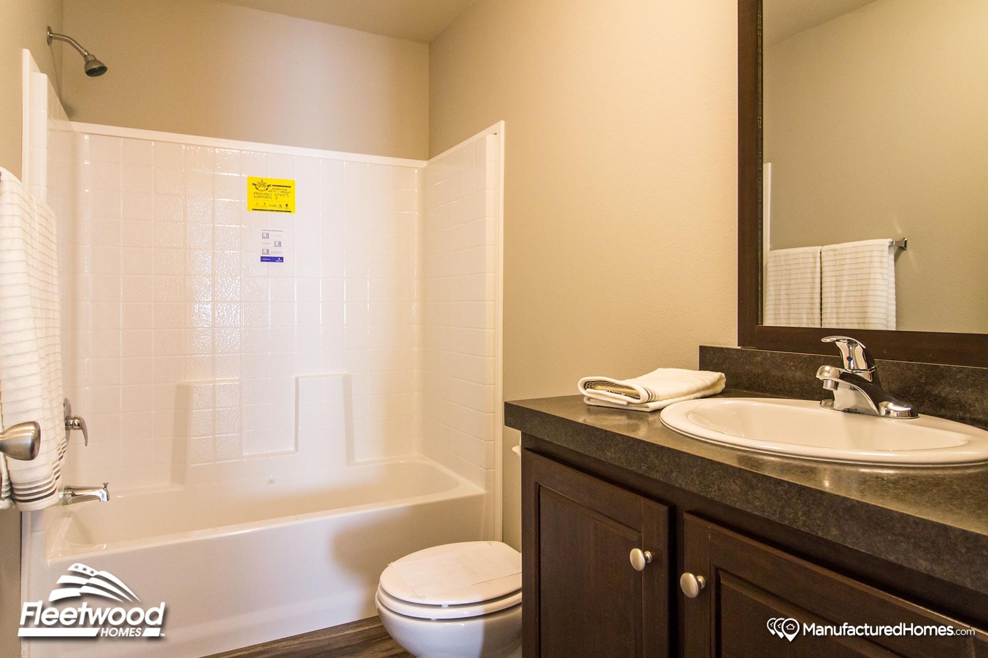 Compact bathroom with a white tile shower-tub combo, dark wood vanity, and a simple countertop sink with a large mirror above.