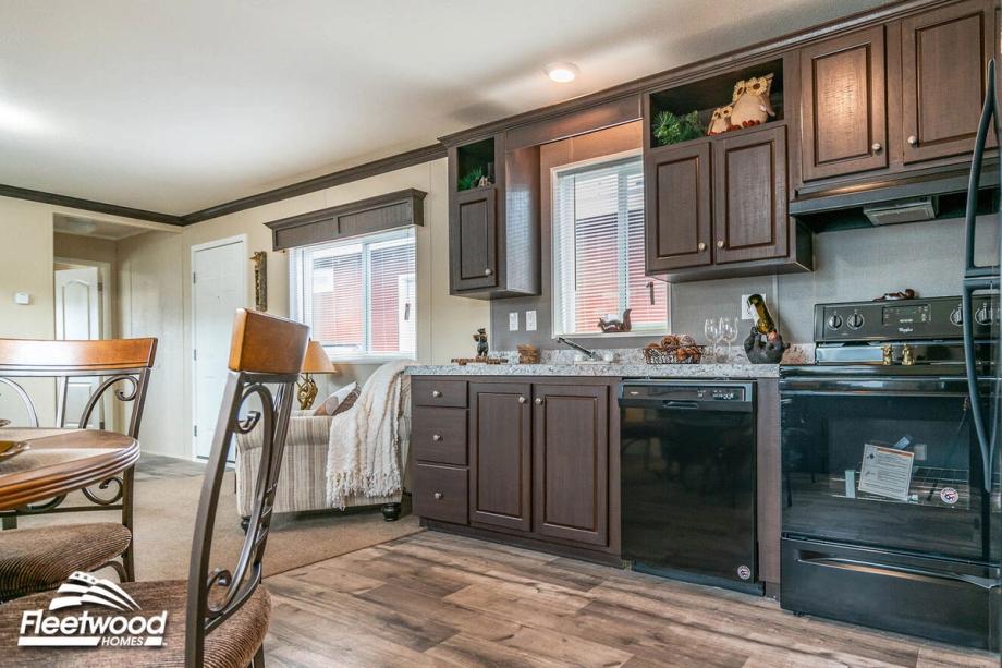 Dining area with a round table and chairs next to a kitchen featuring dark wood cabinets, granite-style countertops, and black appliances.