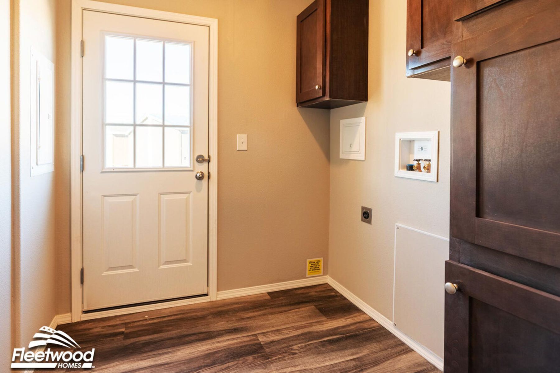 Utility room with wood-look flooring, dark cabinets, washer and dryer hookups, and a white door with window panels.