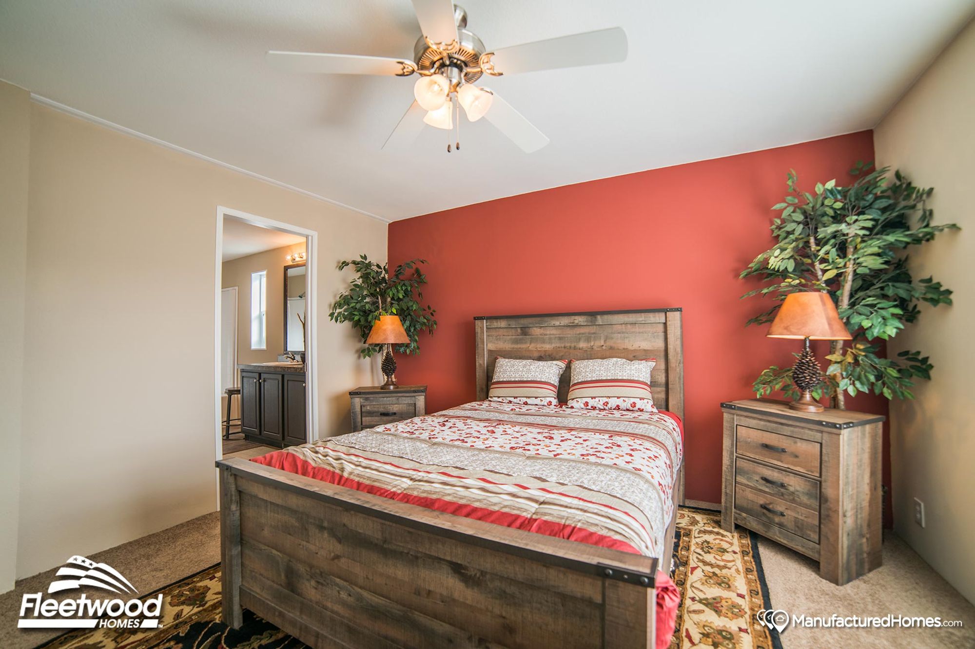 Rustic bedroom with a wooden bed frame and matching nightstands, featuring a red accent wall, floral bedding, and warm lighting from pinecone-themed lamps.